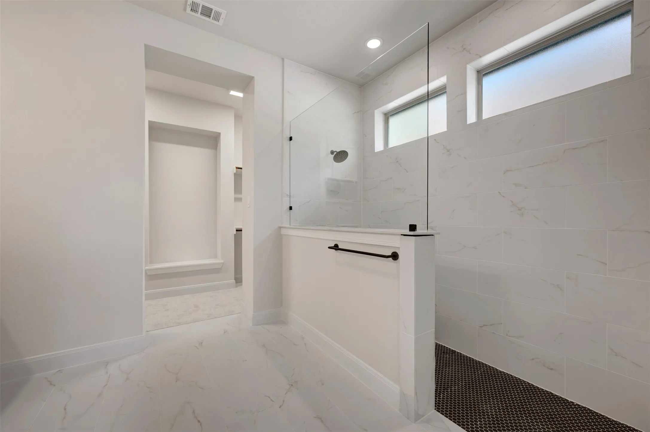 Walk-in shower with clear glass partition, white tile walls, and dark penny tile flooring
