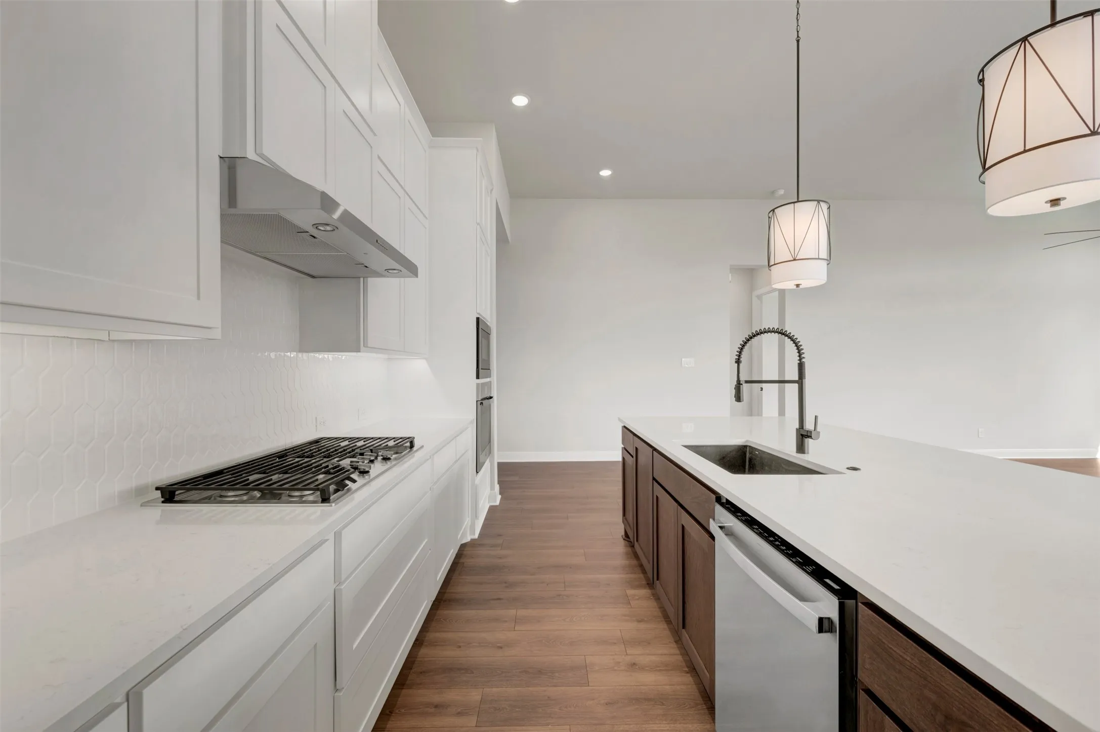 Kitchen featuring white shaker-style cabinetry, a built-in gas range with an overhead vent, white hexagon tile backsplash, and a center island with a stainless steel sink and integrated dishwasher