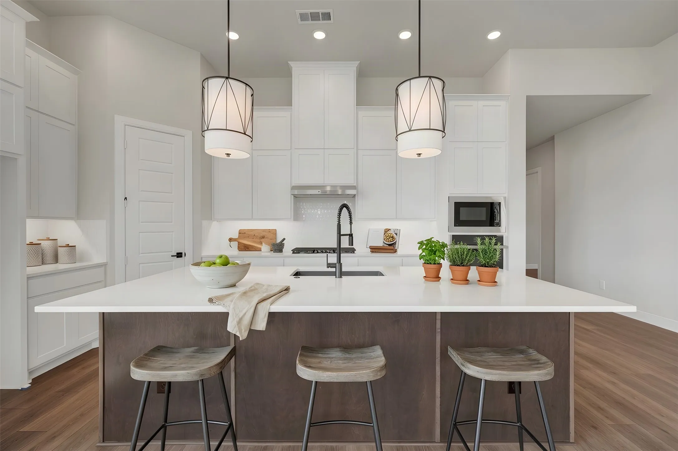 Kitchen featuring an expansive island with a white countertop, wood-finish flooring, white cabinetry, integrated microwave, and pendant lighting