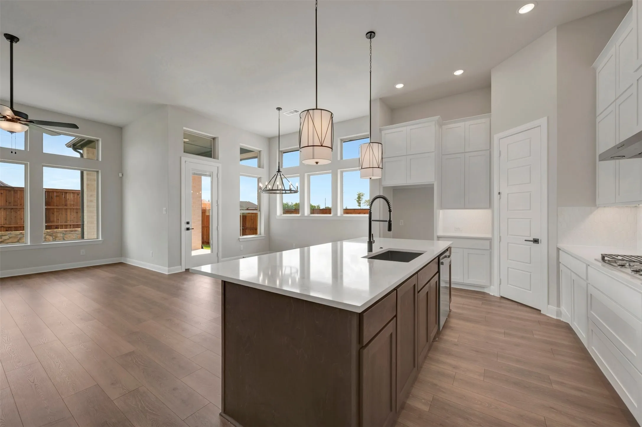 Open-concept living space featuring wood-finish flooring, a kitchen island with a built-in sink, white cabinetry, and multiple large windows