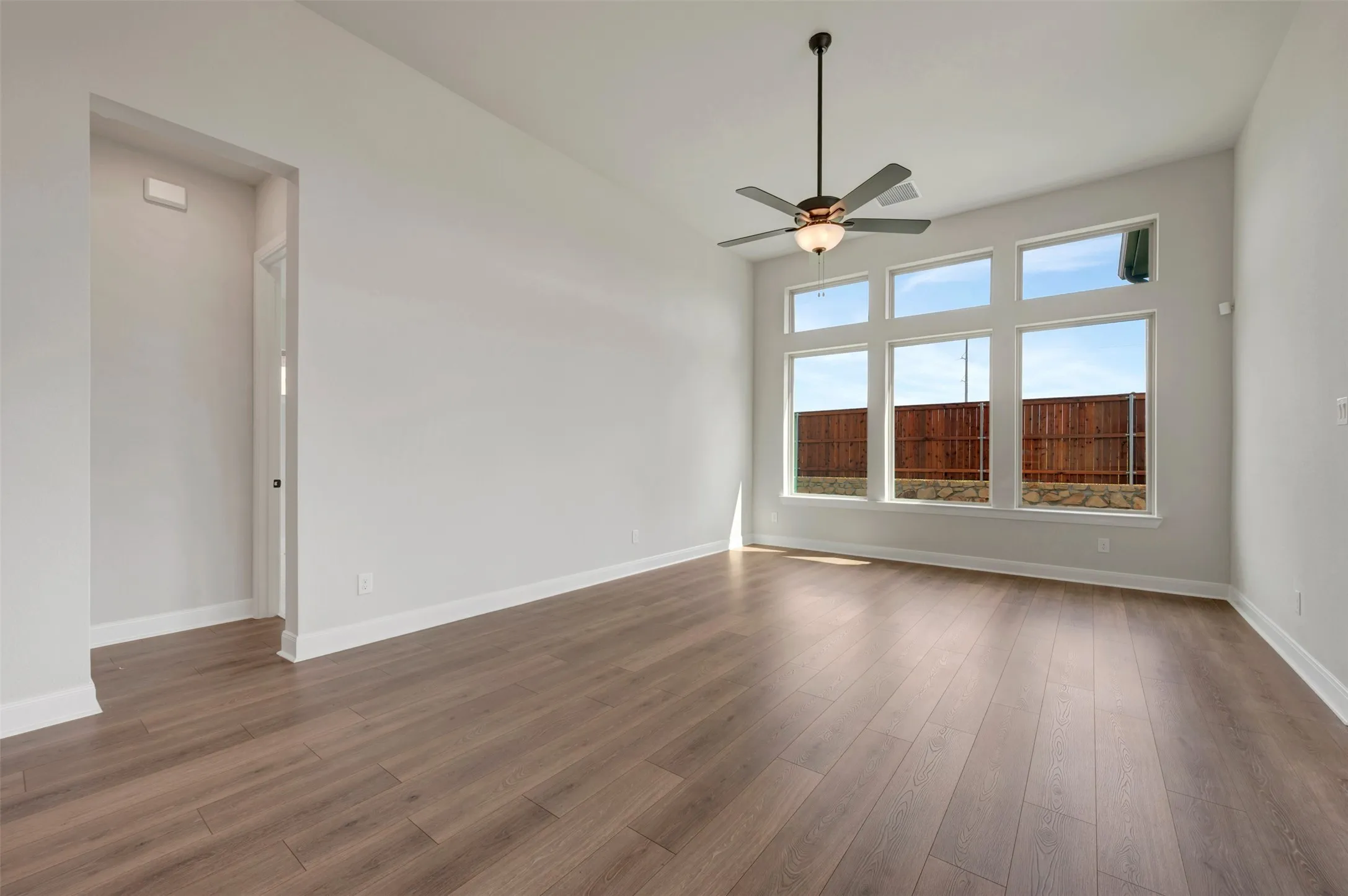 Spacious room featuring high ceilings, wood-finish flooring, a contemporary ceiling fan, and large windows
