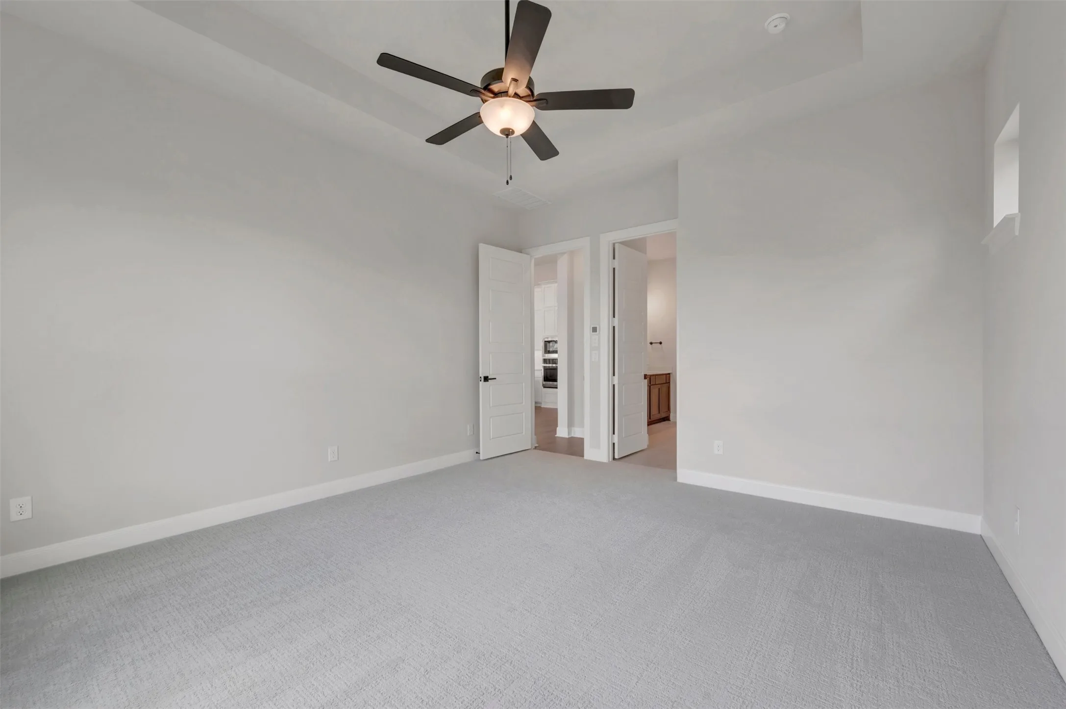 Recessed ceiling with a central ceiling fan, light gray carpeting, neutral wall paint, and white trim