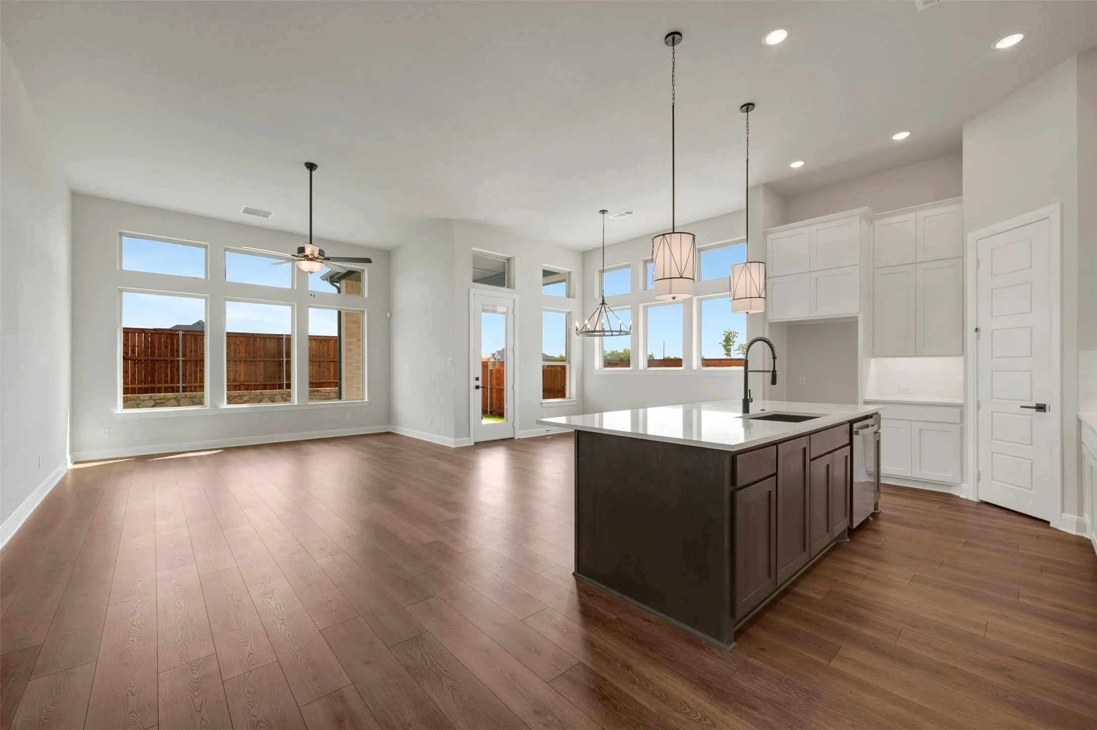Open-concept living area featuring wood-finish flooring, a kitchen island with stone countertop, white shaker-style cabinetry, and large windows