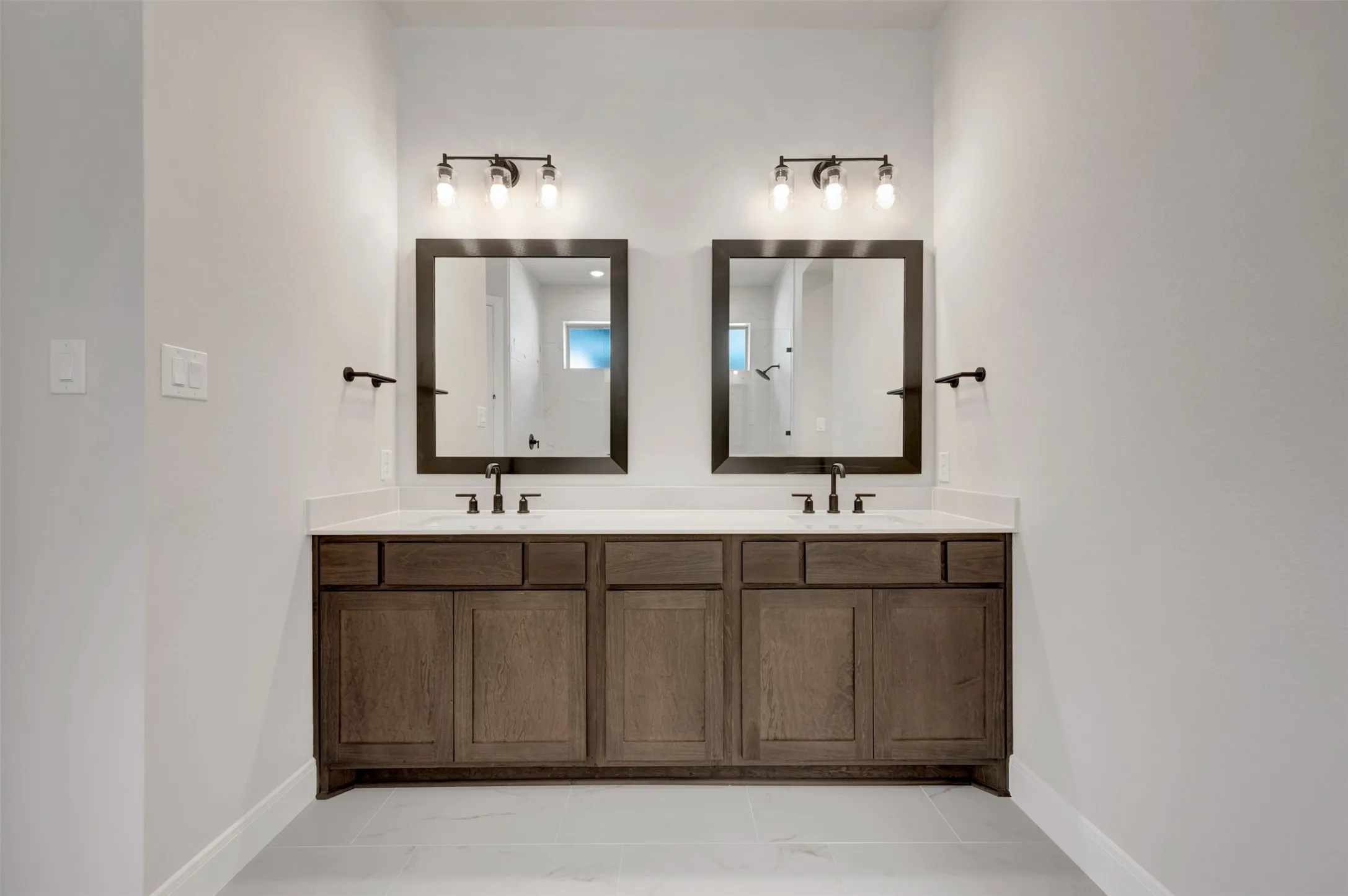 Dual vanities with wood-finish cabinetry, integrated sinks, white countertops, and framed mirrors