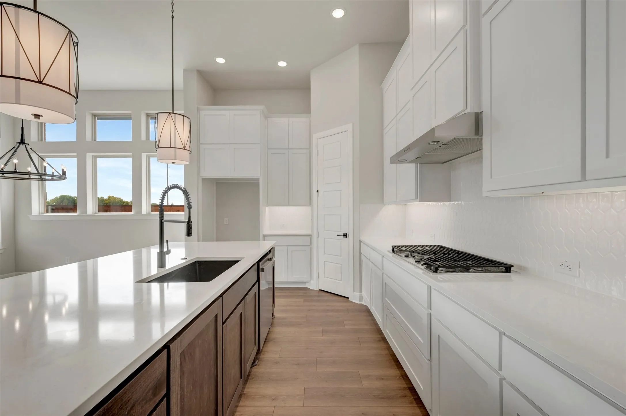 Kitchen featuring an island with an undermount sink, a gas cooktop with an overhead range hood, white cabinetry, wood-finish flooring, and recessed lighting