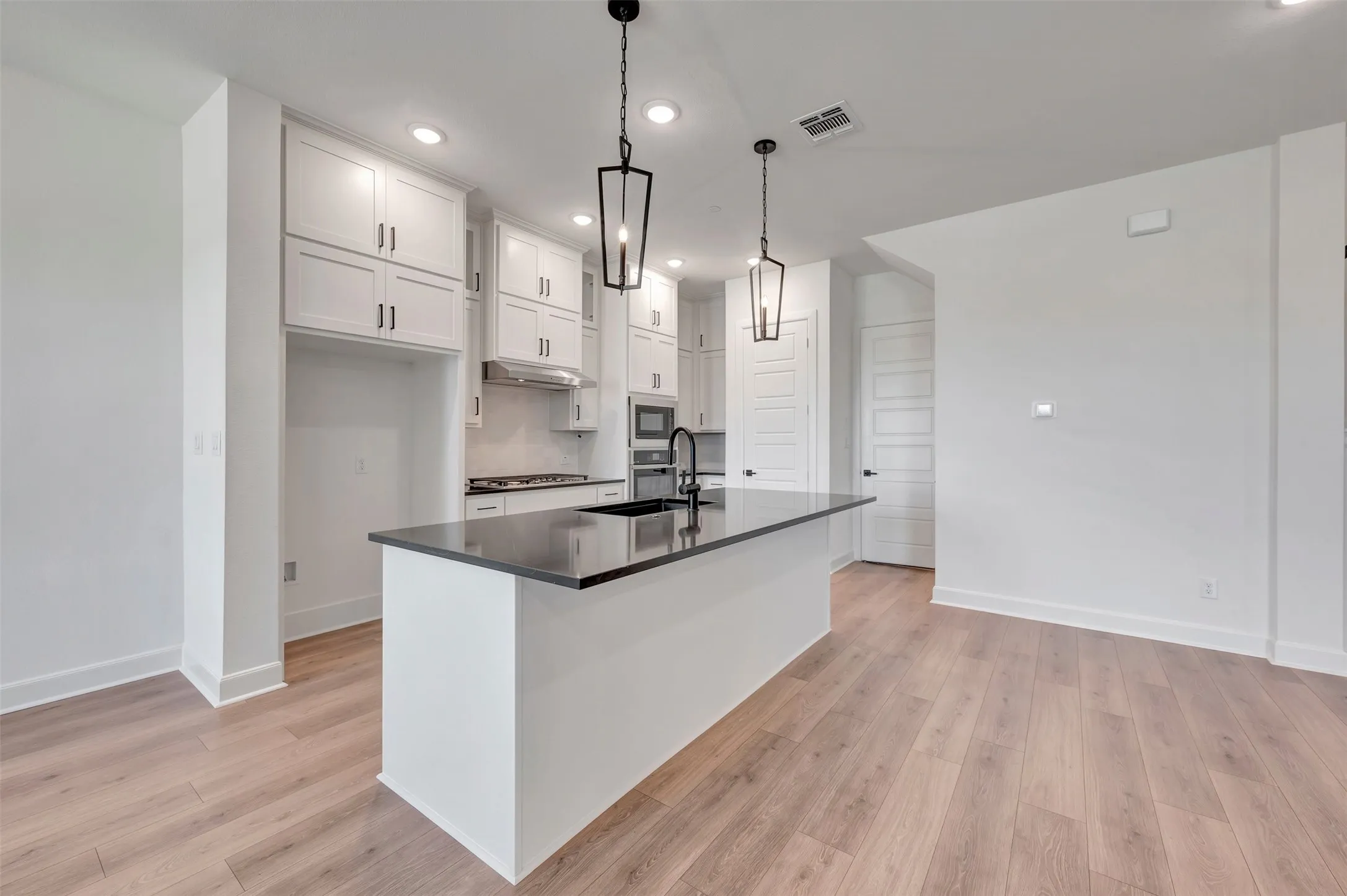 Modern kitchen featuring a dark countertop island with pendant lighting, white cabinetry, a built-in oven, and wood-finish flooring