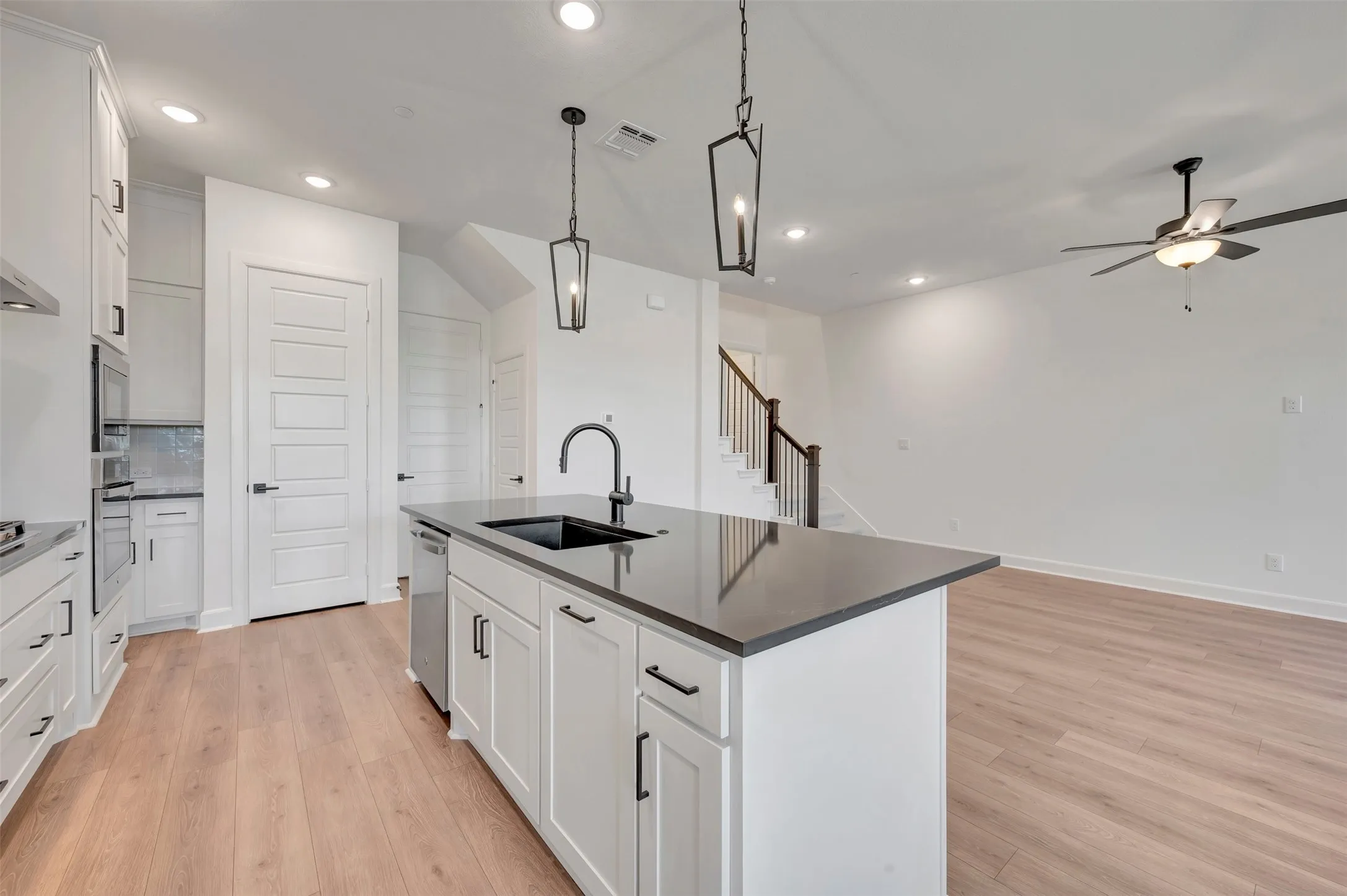 Open-concept kitchen featuring a large island with a dark countertop and sink, white cabinetry with black hardware, wood-finish flooring, and recessed lighting