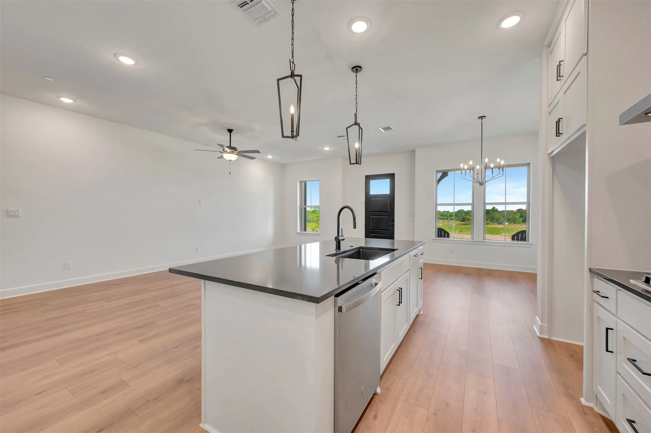 Open-concept living space featuring a central kitchen island with a black sink and faucet, integrated dishwasher, and pendant lighting