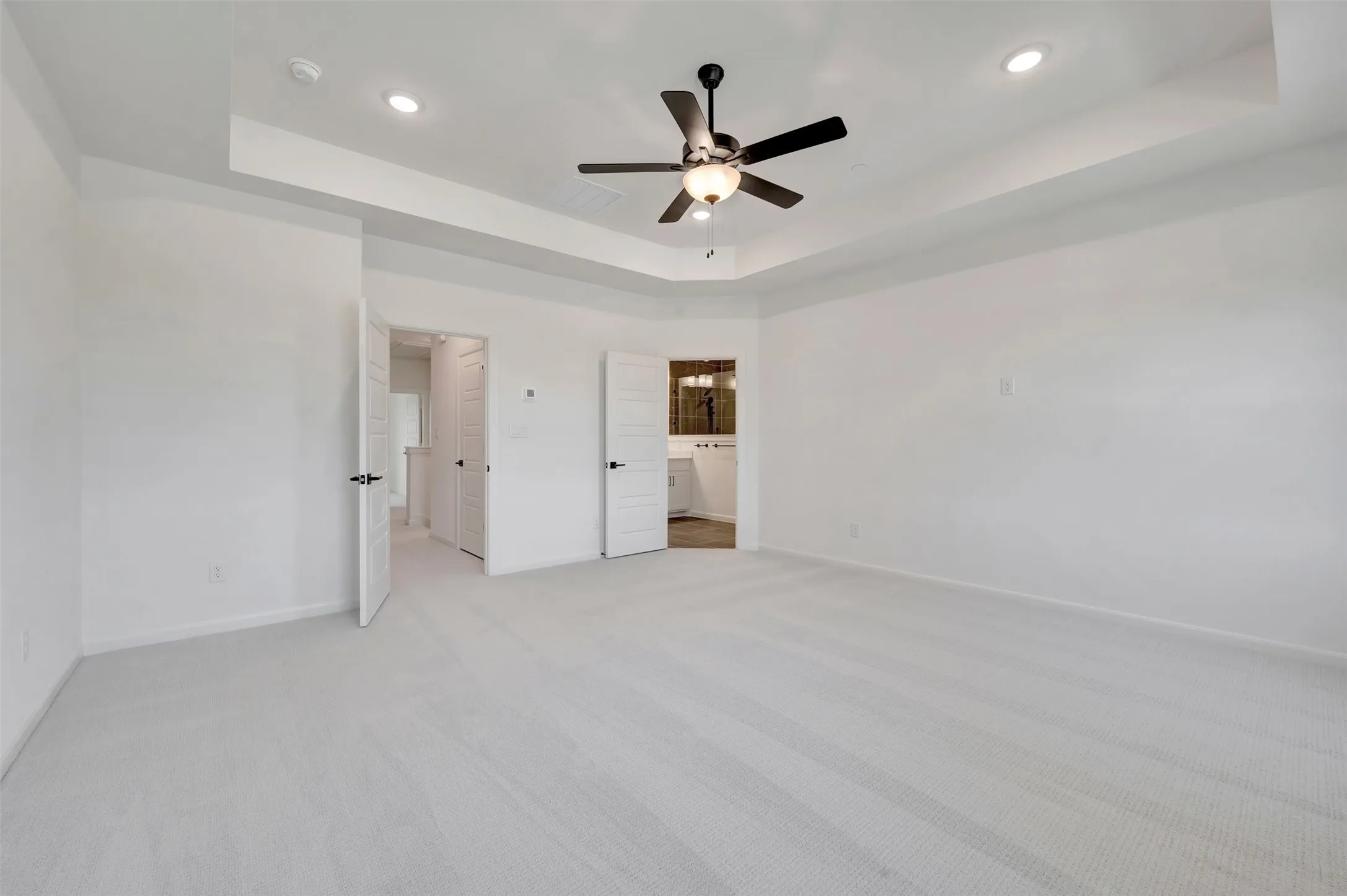 Spacious room featuring light-toned carpet flooring, a tray ceiling with recessed lighting, and a ceiling fan with light fixture