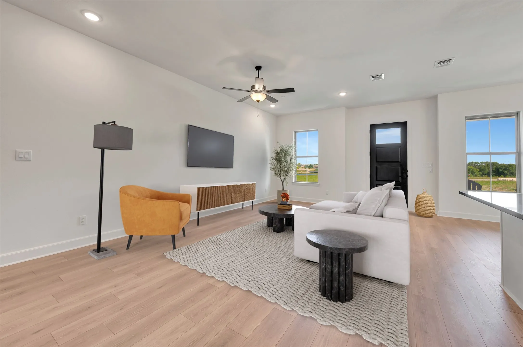 Spacious living area featuring light wood-finish flooring, a contemporary ceiling fan with integrated lighting, and recessed ceiling lights