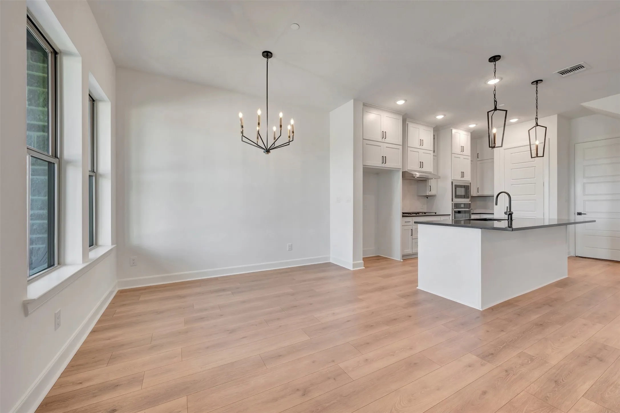 Open-concept living space featuring wood-finish flooring, a modern kitchen island with an undermount sink, pendant lighting, and a contemporary chandelier