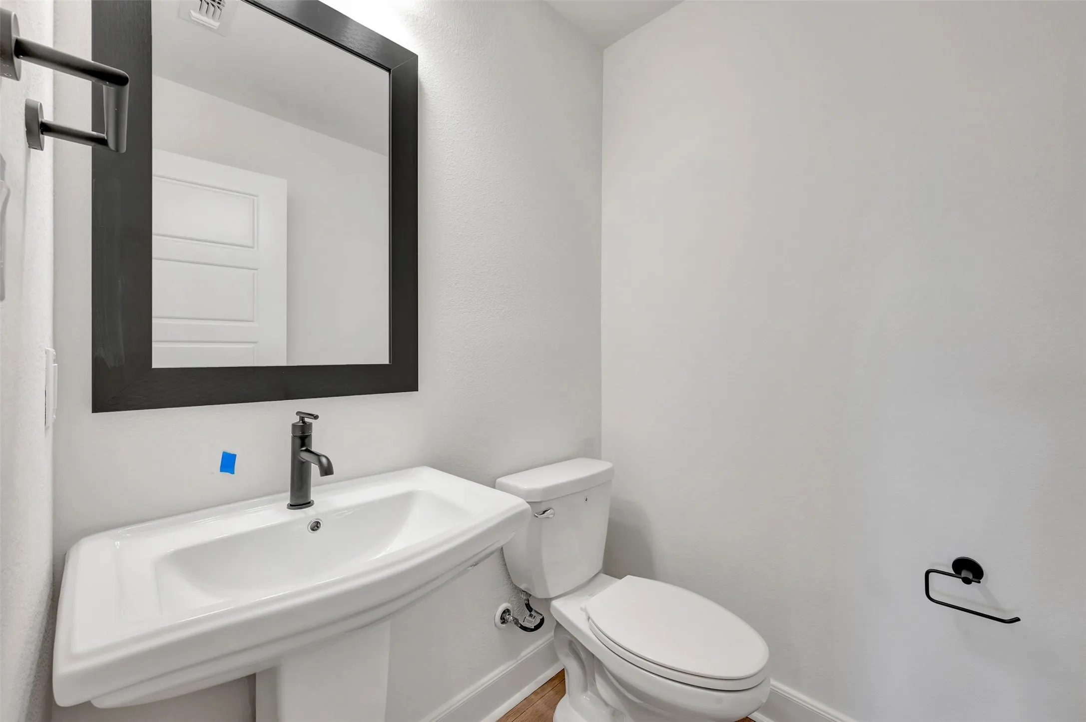 Pedestal sink with matte black faucet and framed mirror