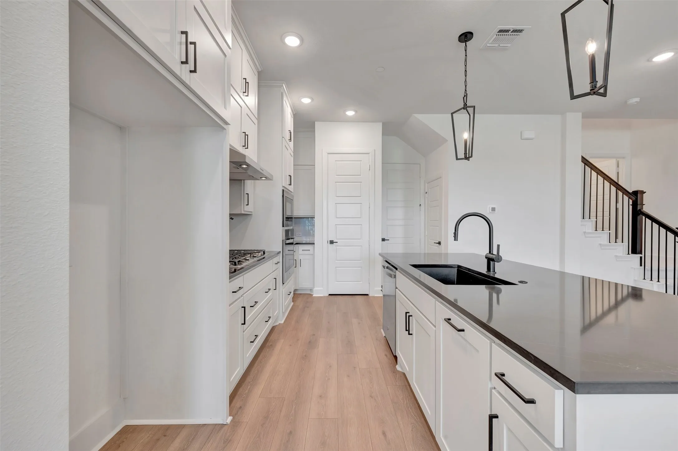 Spacious kitchen featuring white cabinetry with matte black hardware, wood-finish flooring, a large island with an undermount sink and dark countertop, stainless steel appliances, and recessed lighting