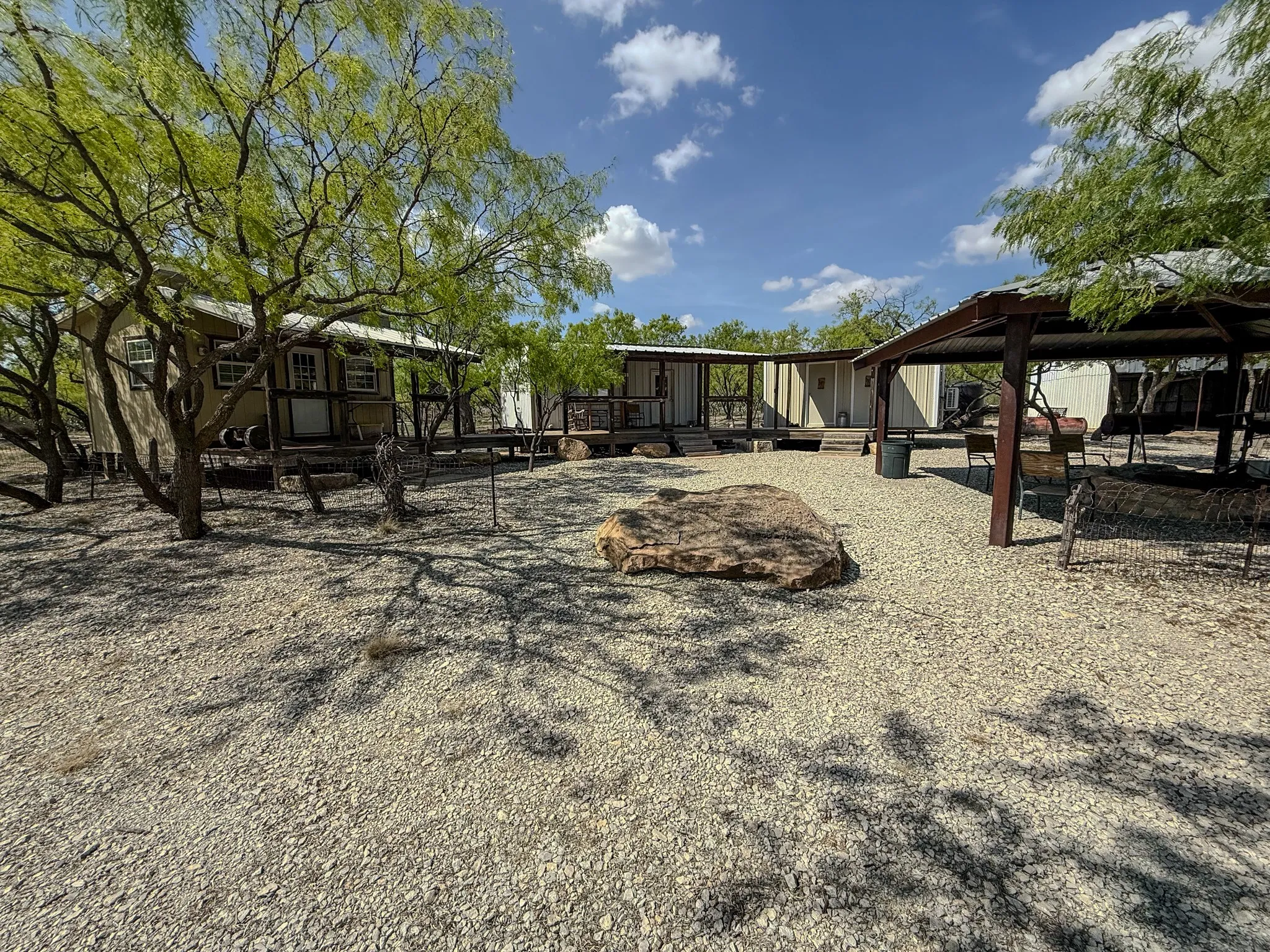 Expansive gravel courtyard featuring mature trees and a substantial stone accent