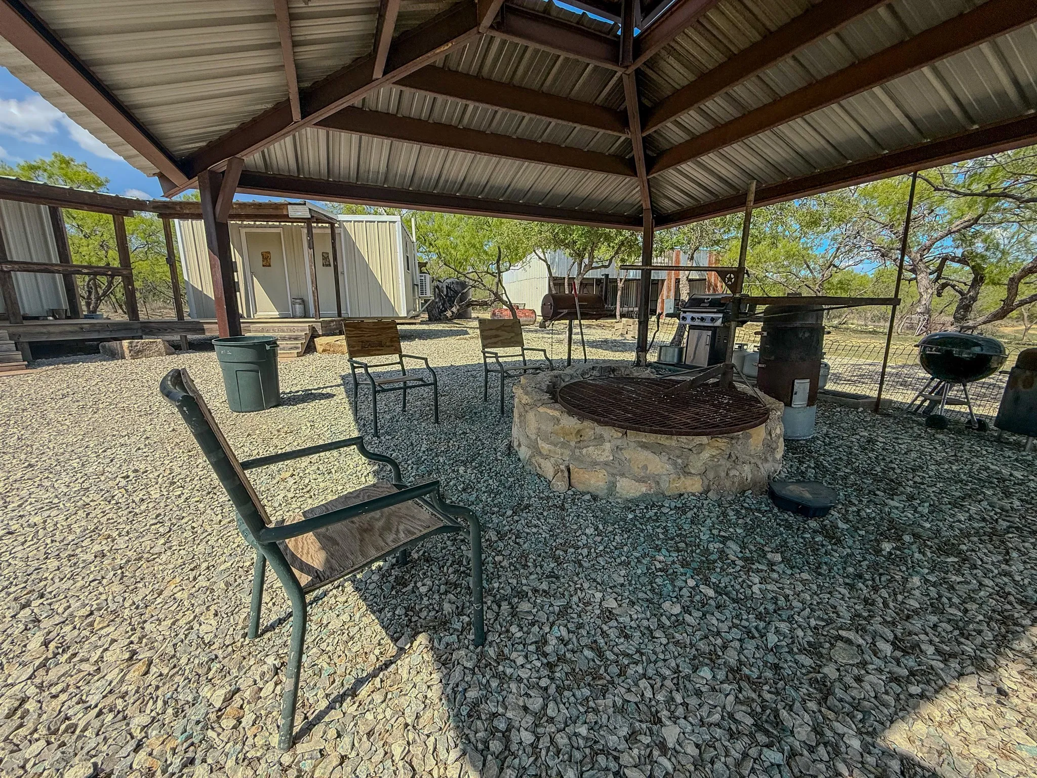 Covered outdoor living area with a stone fire pit, corrugated metal roof, and exposed metal beam construction