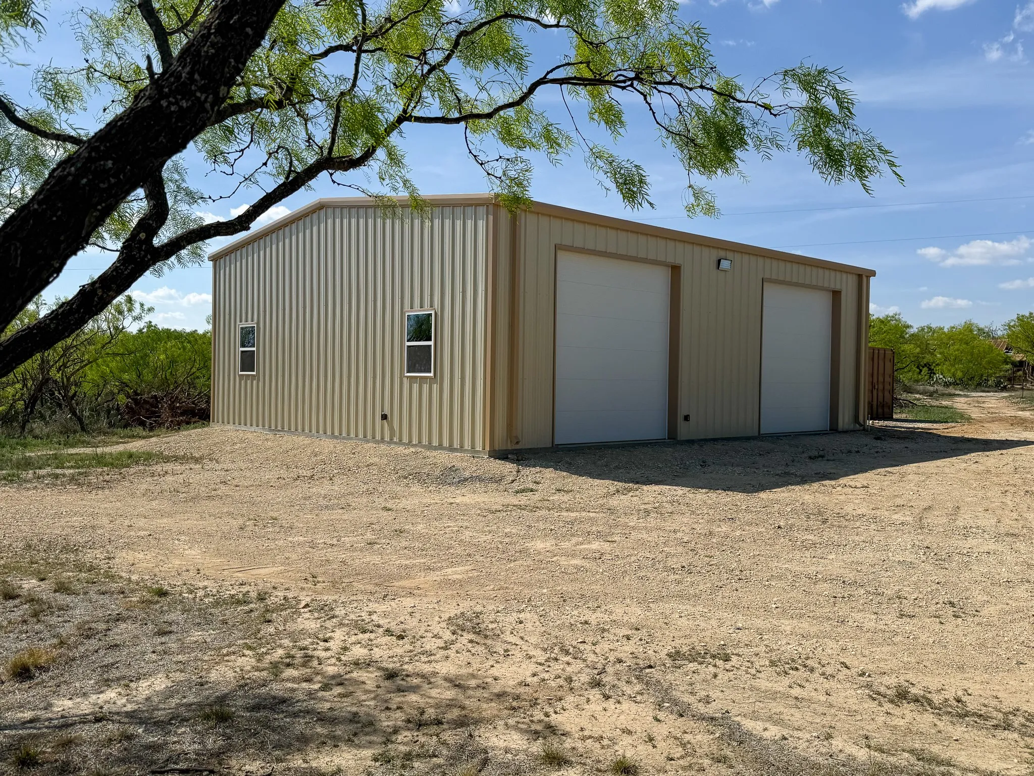 Newly constructed metal building featuring two roll-up garage doors, a concrete foundation, exterior lighting, and multiple windows