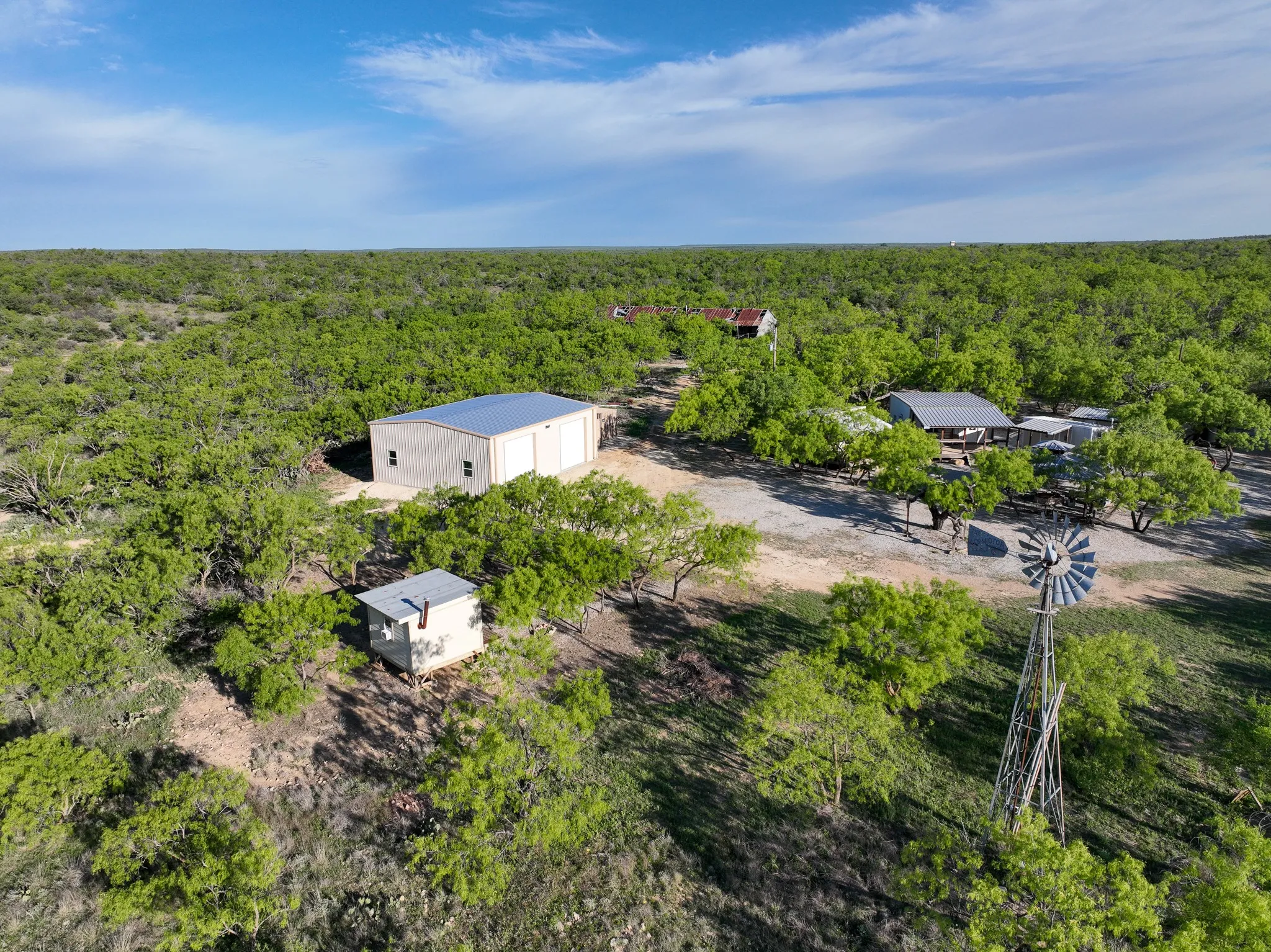 Aerial property overview featuring multiple structures surrounded by extensive tree coverage