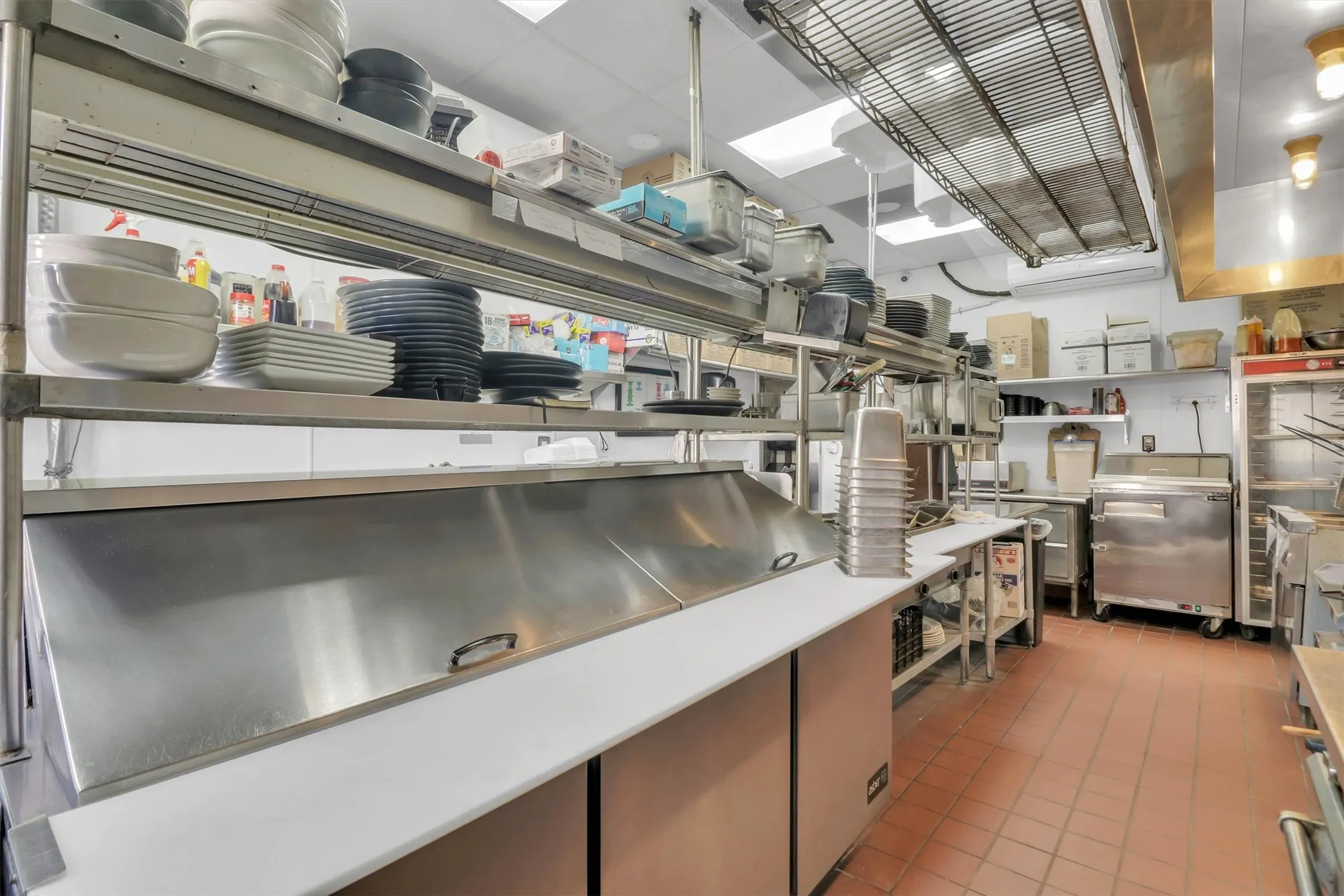 Commercial kitchen featuring extensive stainless steel surfaces, integrated refrigeration units, and durable tile flooring
