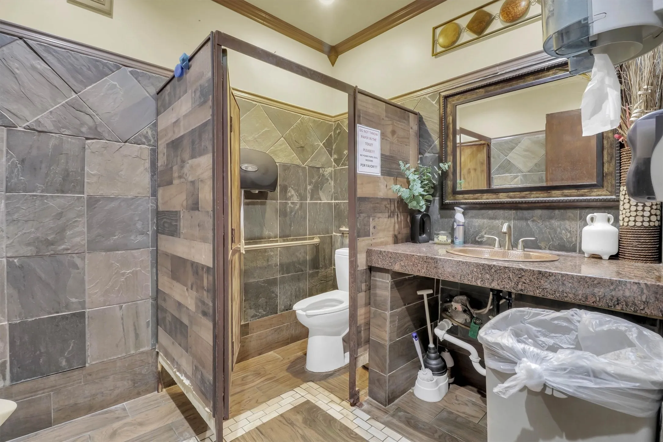 Stone-tiled bathroom featuring a built-in vanity with a copper-toned sink and a decorative framed mirror