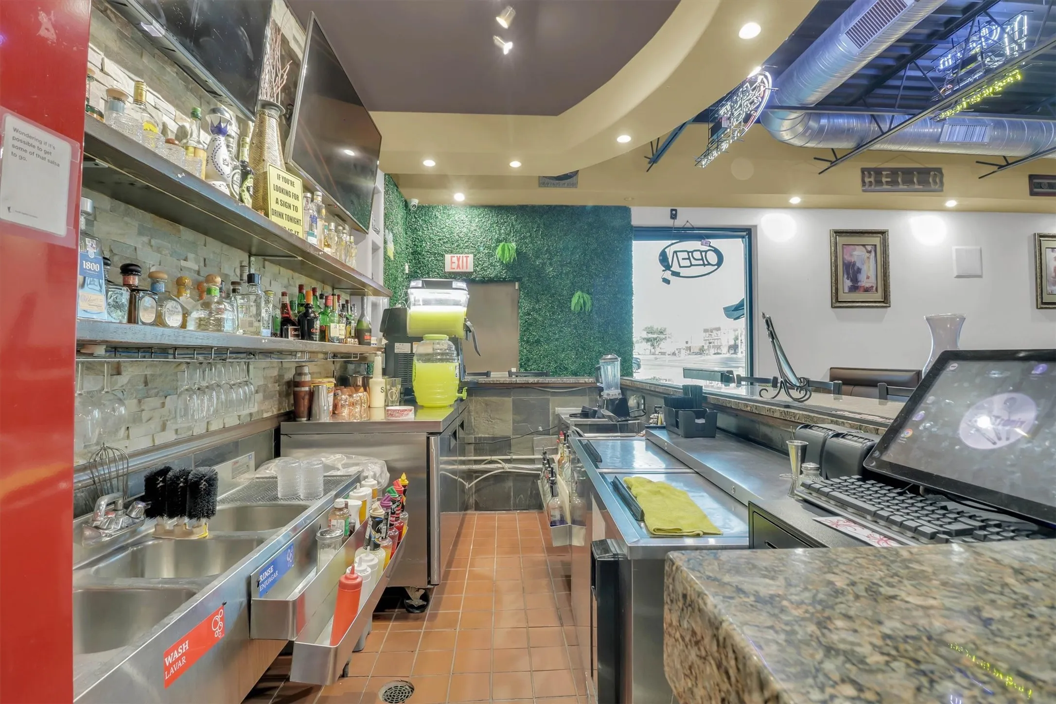 Commercial bar space featuring a three-compartment sink, stainless steel shelving, and a granite-look countertop