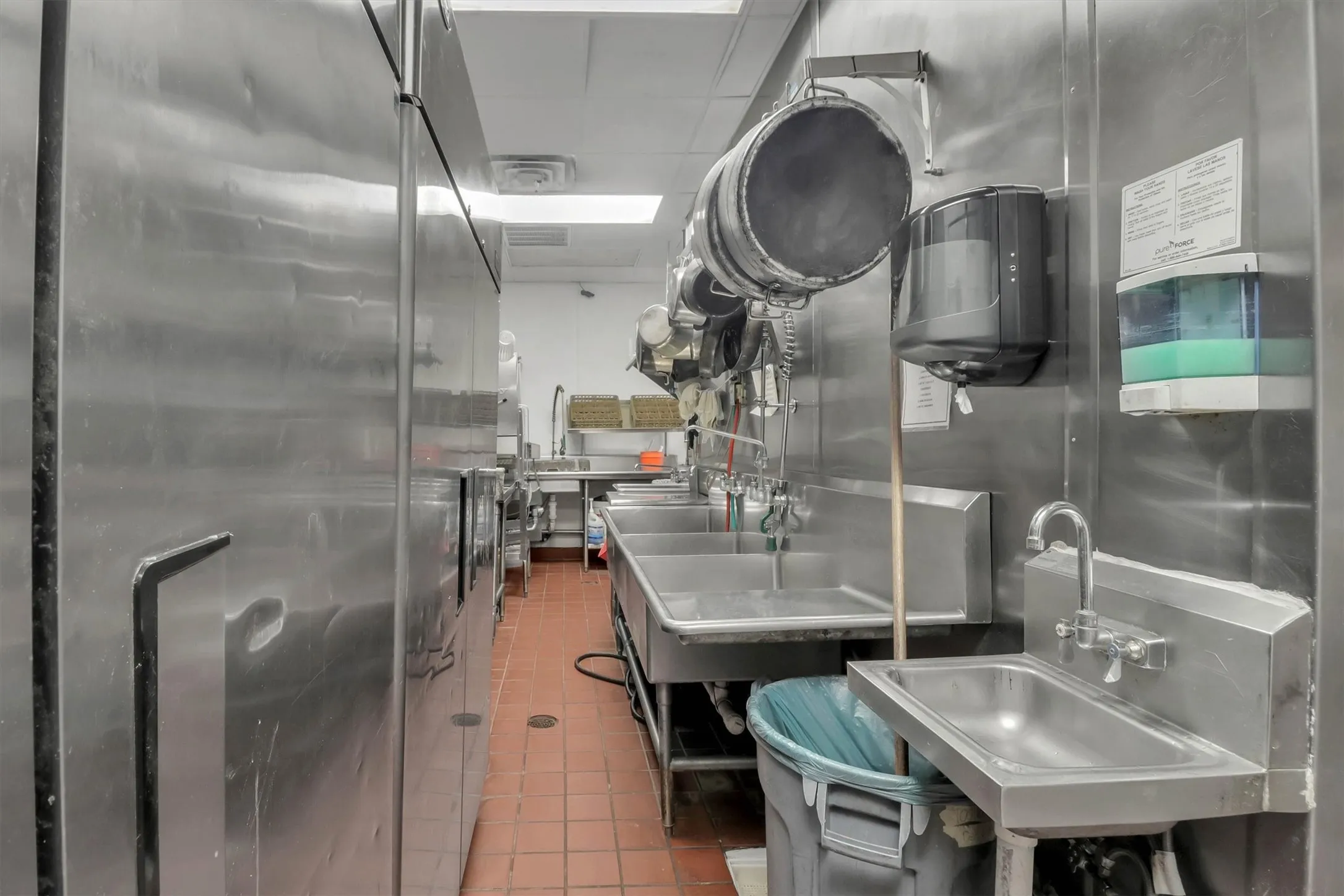 Commercial kitchen featuring stainless steel appliances, multiple utility sinks, and durable tile flooring