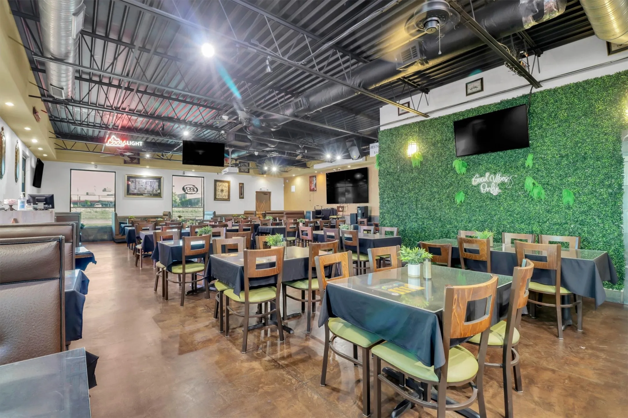Spacious commercial interior featuring exposed industrial ceiling, expansive window openings, and a decorative green wall paneling