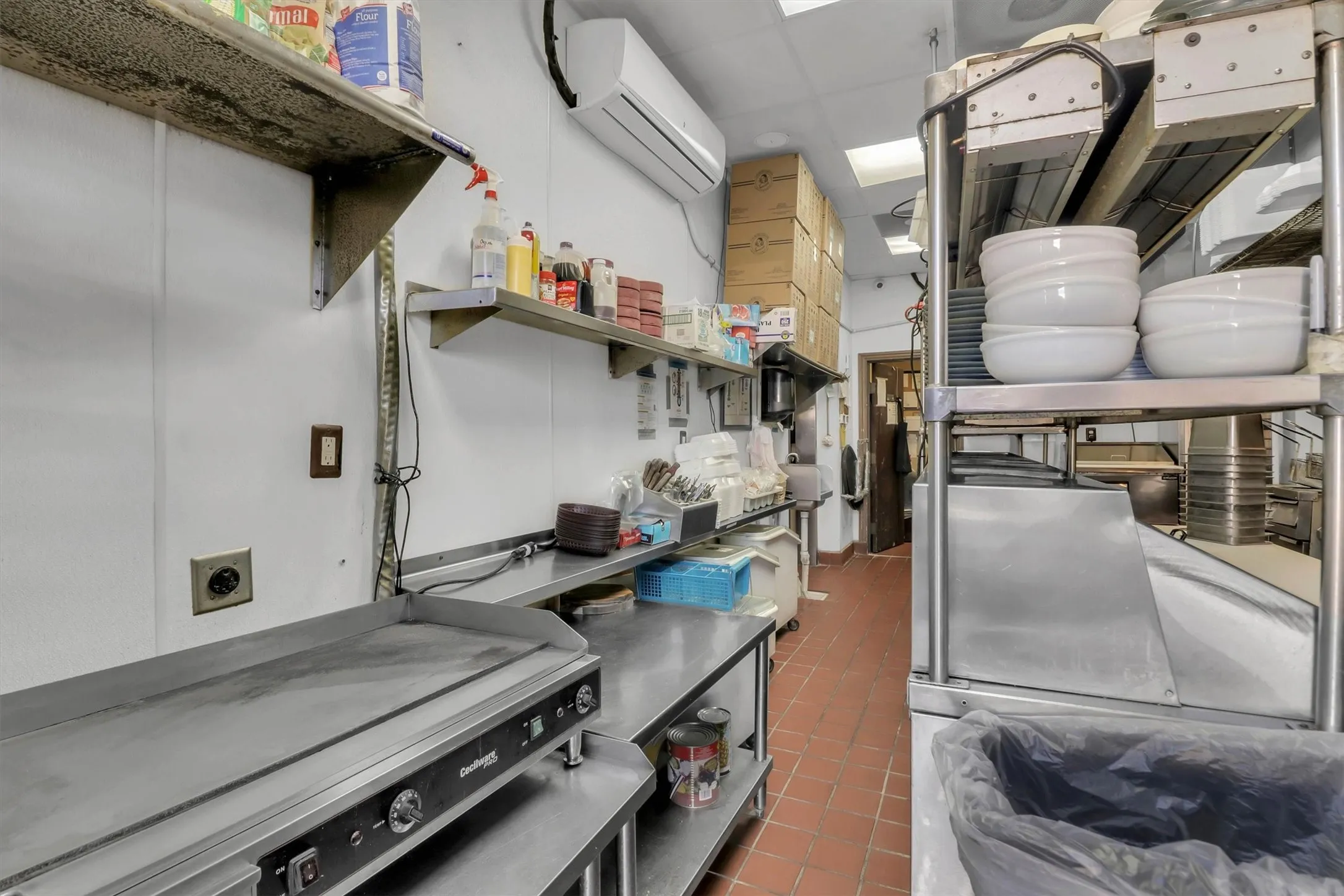 Commercial kitchen featuring stainless steel prep surfaces, wall-mounted shelving, a flat-top griddle, and tile flooring