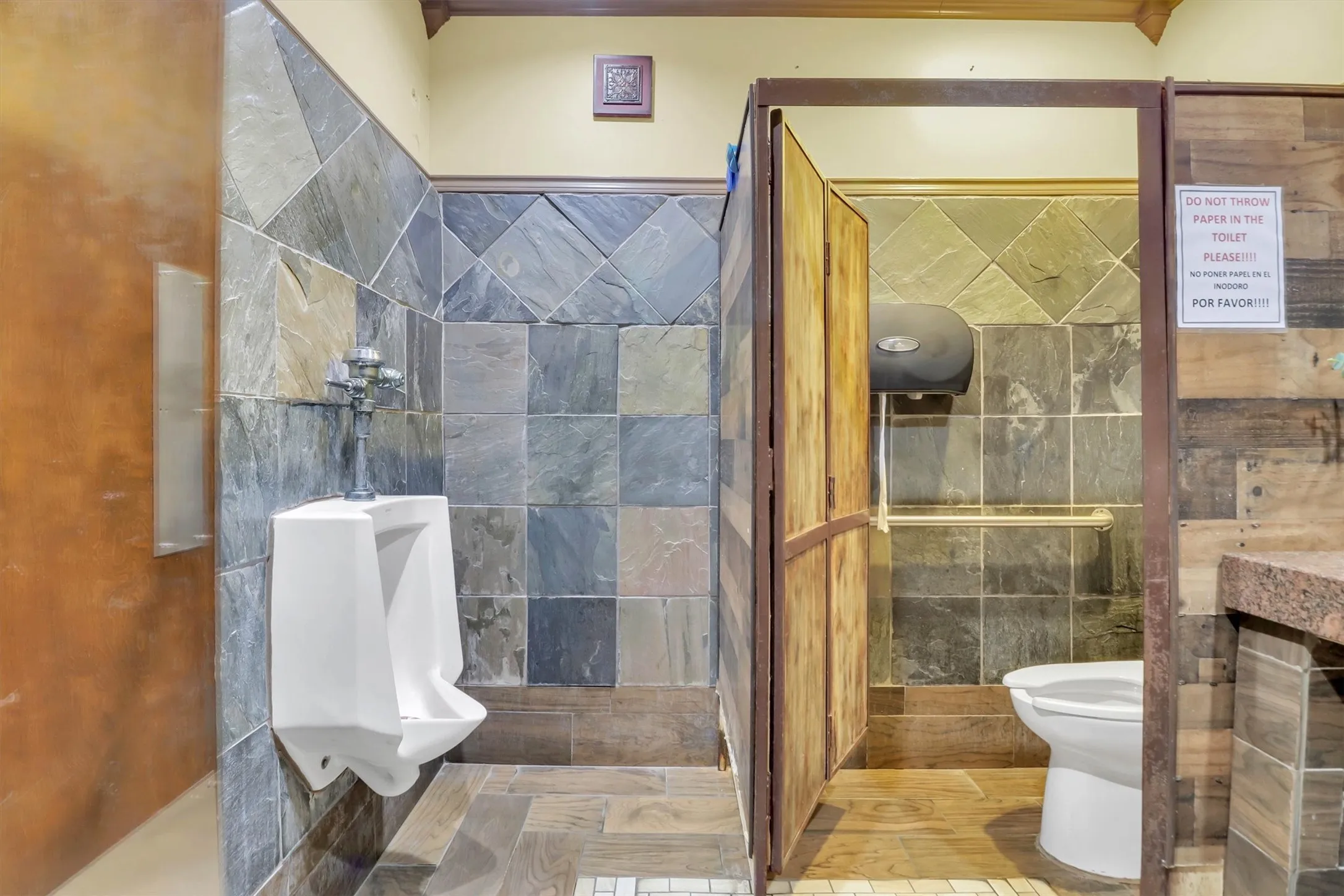 Restroom featuring slate tile walls, wood-finish flooring, wood panel partitions, and a granite-finish countertop