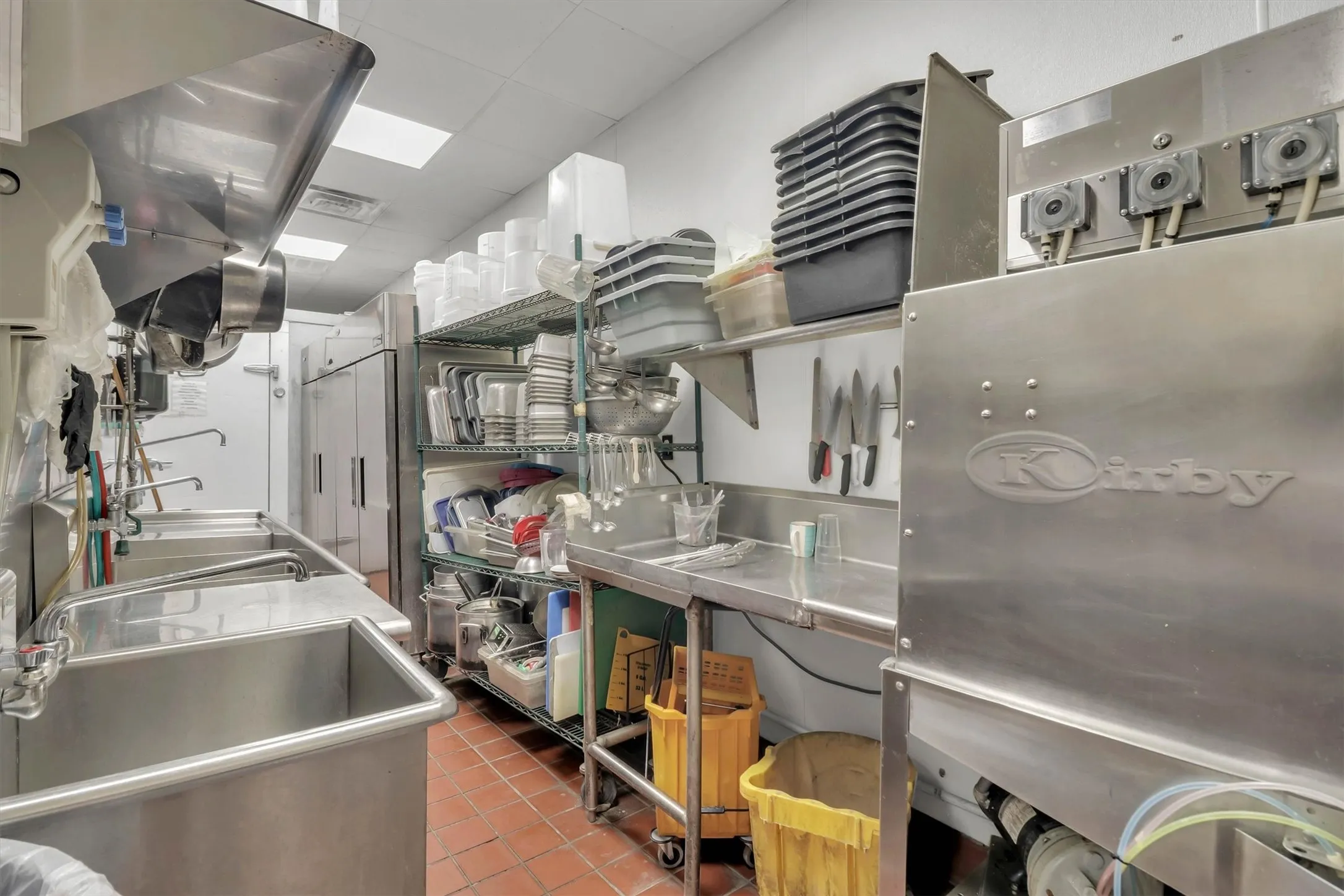 Commercial kitchen featuring multiple stainless steel sinks, industrial shelving, and durable tile flooring