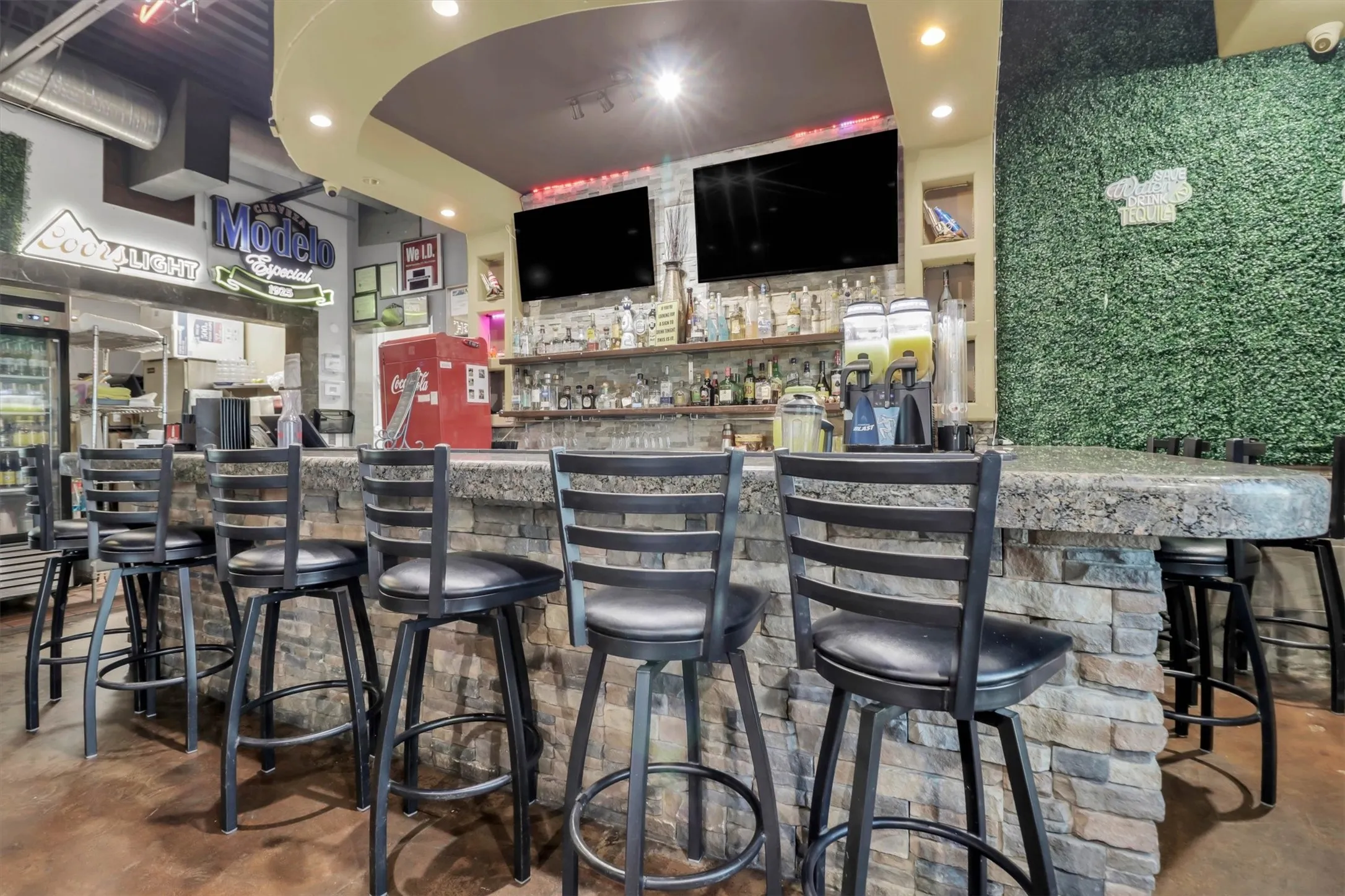 Stone-clad bar featuring a granite-finish countertop, recessed lighting, wall-mounted displays, and a textured green wall accent