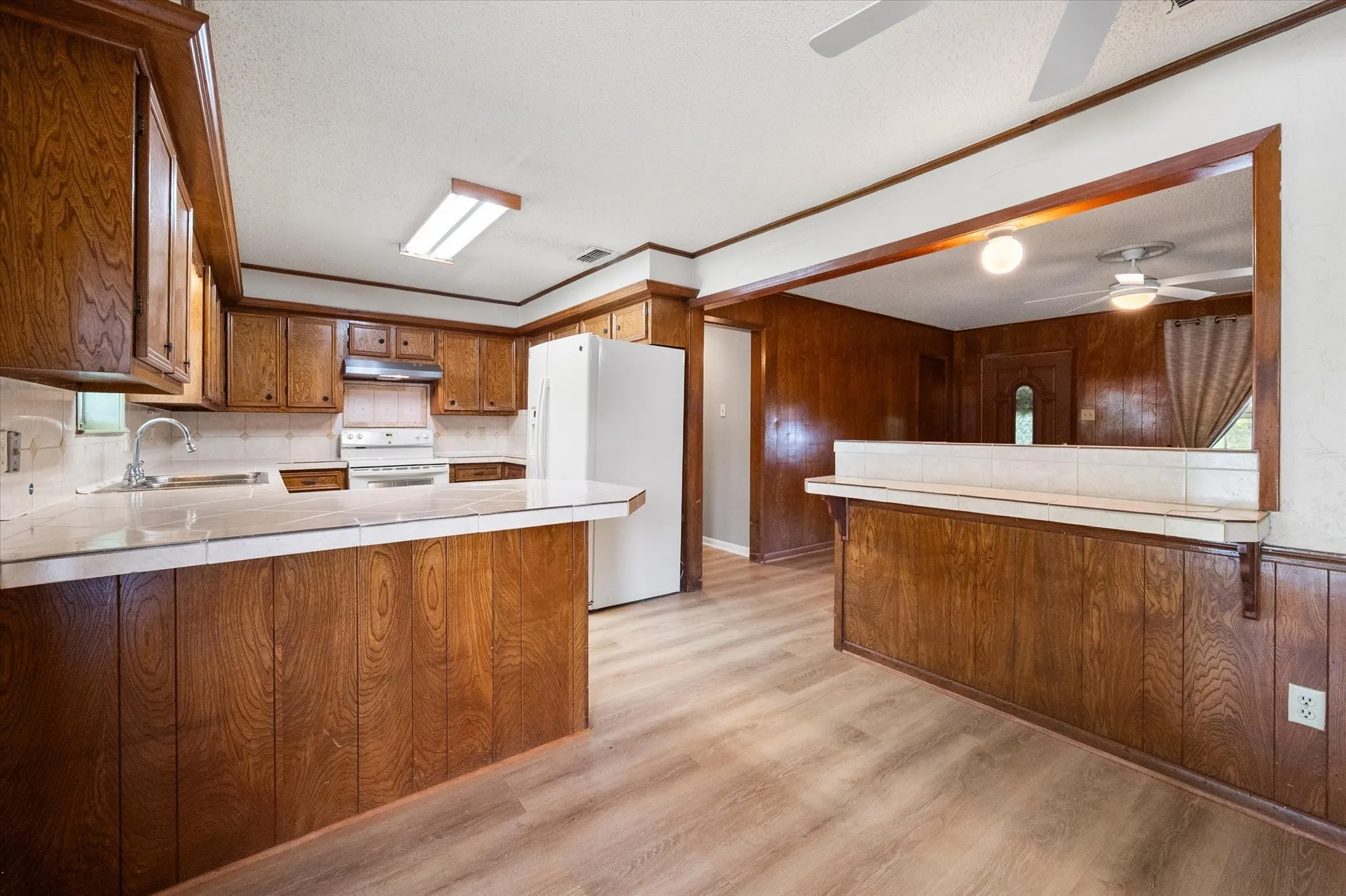 Kitchen featuring wood cabinetry, white appliances, tile countertops, a tile backsplash, and wood-finish flooring
