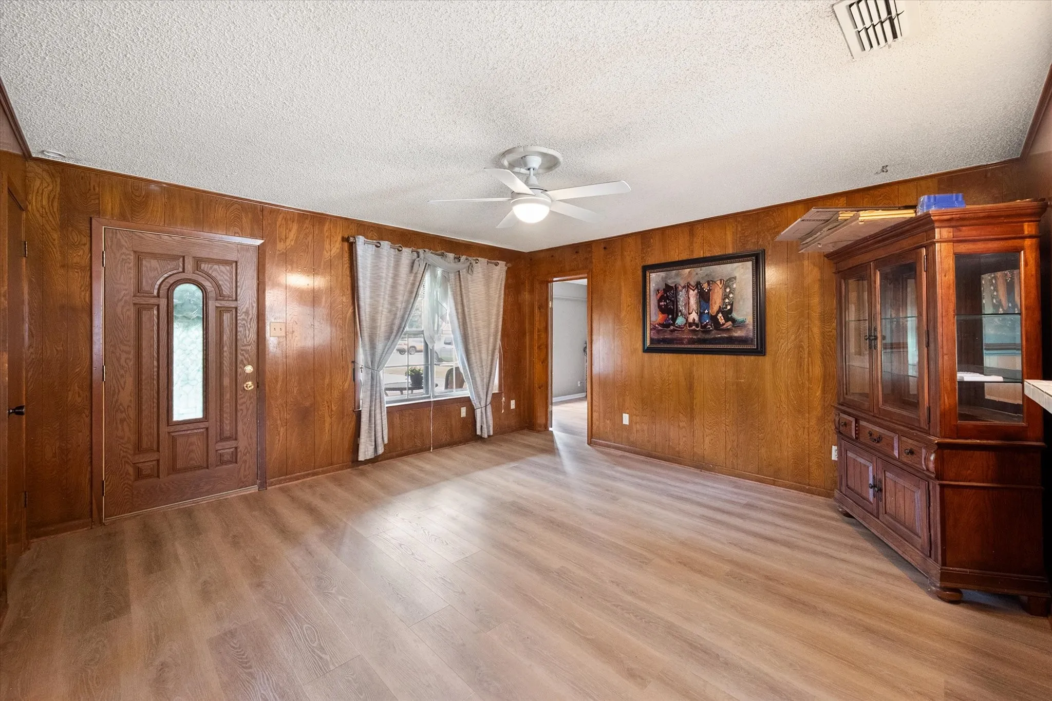 Spacious living area featuring wood-finish paneling, contemporary wood-finish flooring, and a ceiling fan with integrated lighting