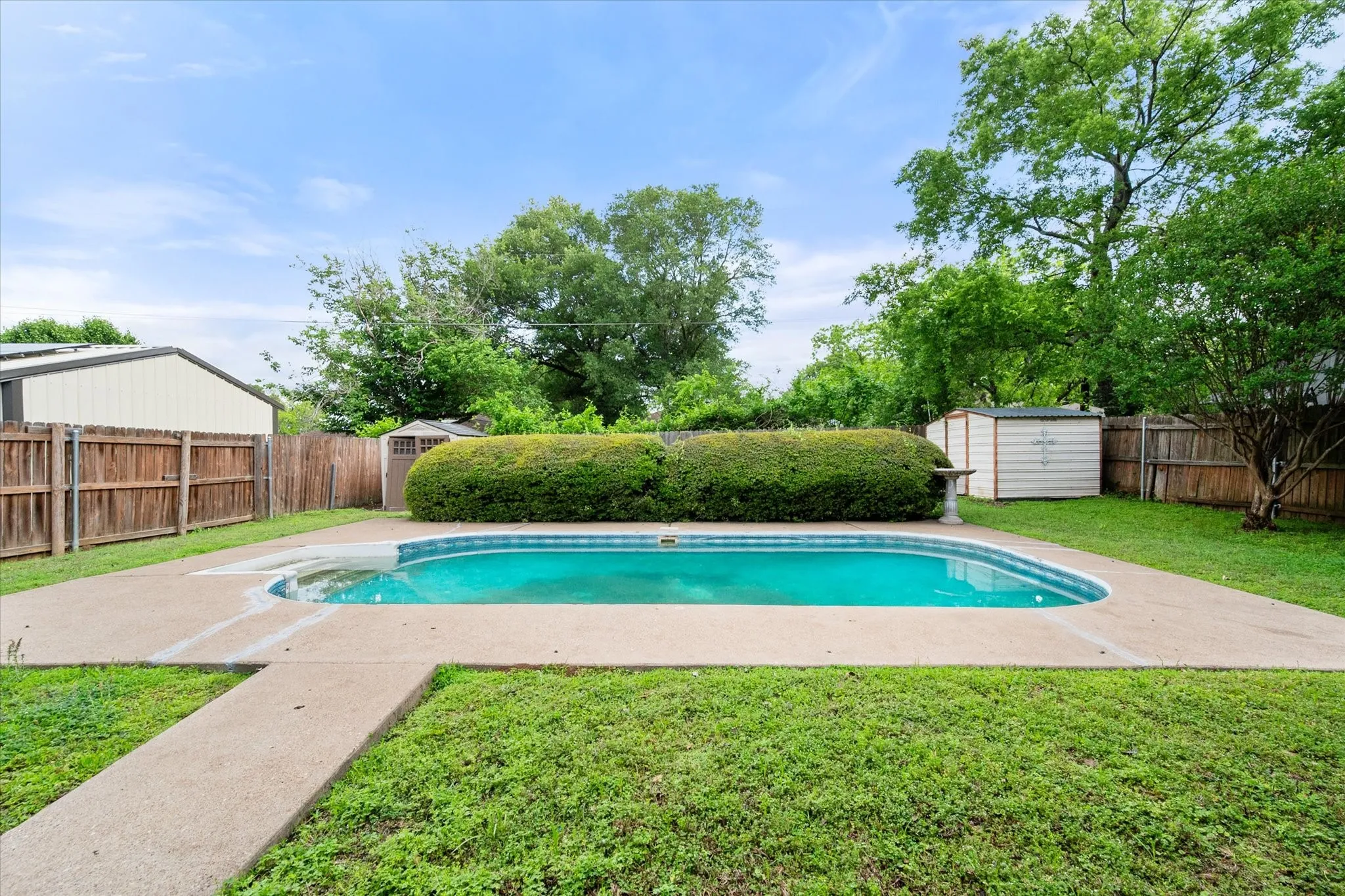 Backyard featuring an in-ground swimming pool with a concrete surround, wood privacy fencing, and mature perimeter landscaping
