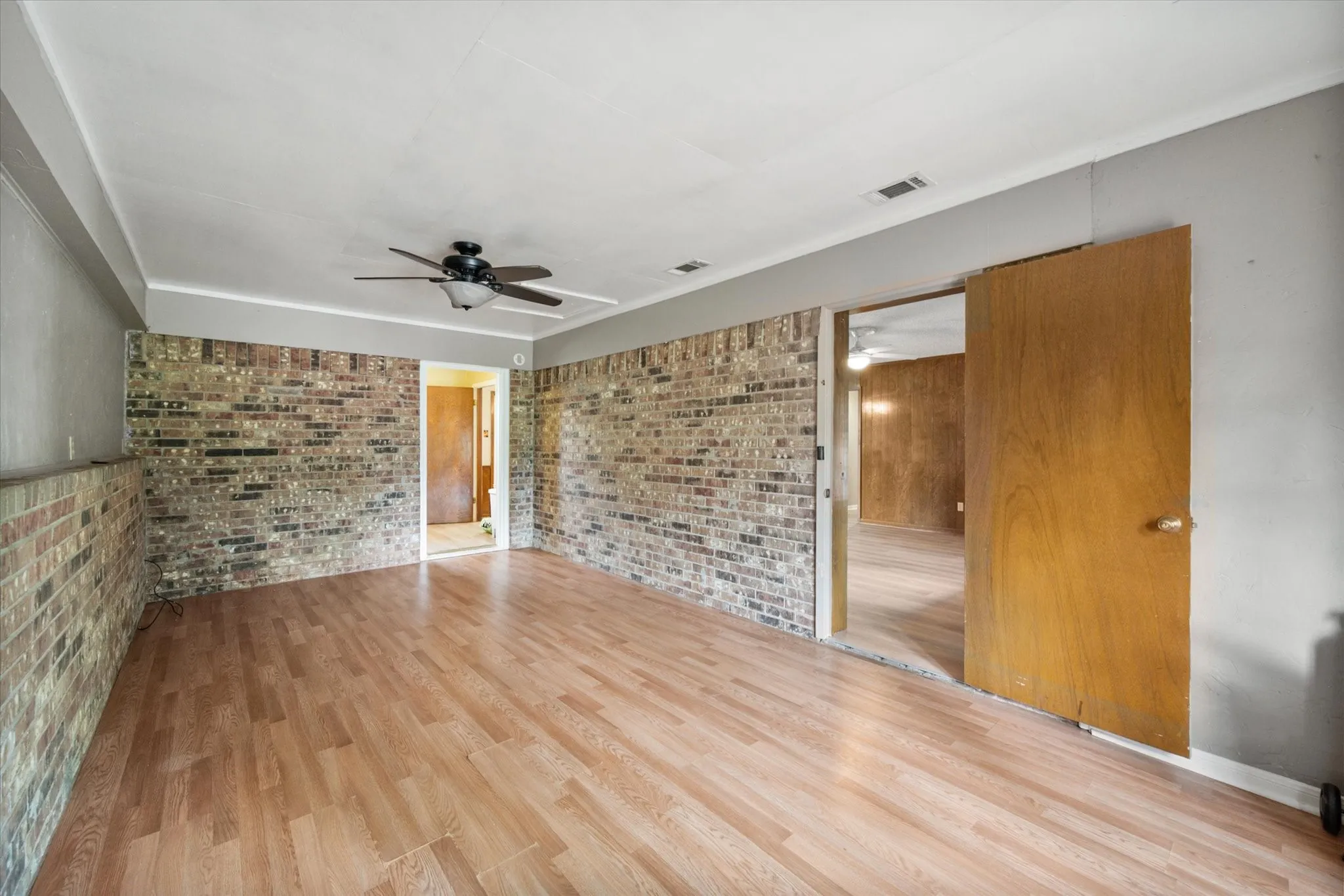 Spacious room featuring wood-finish flooring, exposed brick wall accents, and a ceiling fan with integrated lighting