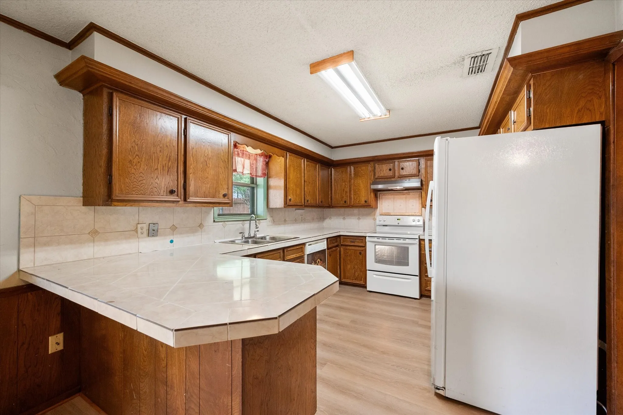 Kitchen featuring wood cabinetry, tile countertops, a tile backsplash, and light wood-finish flooring