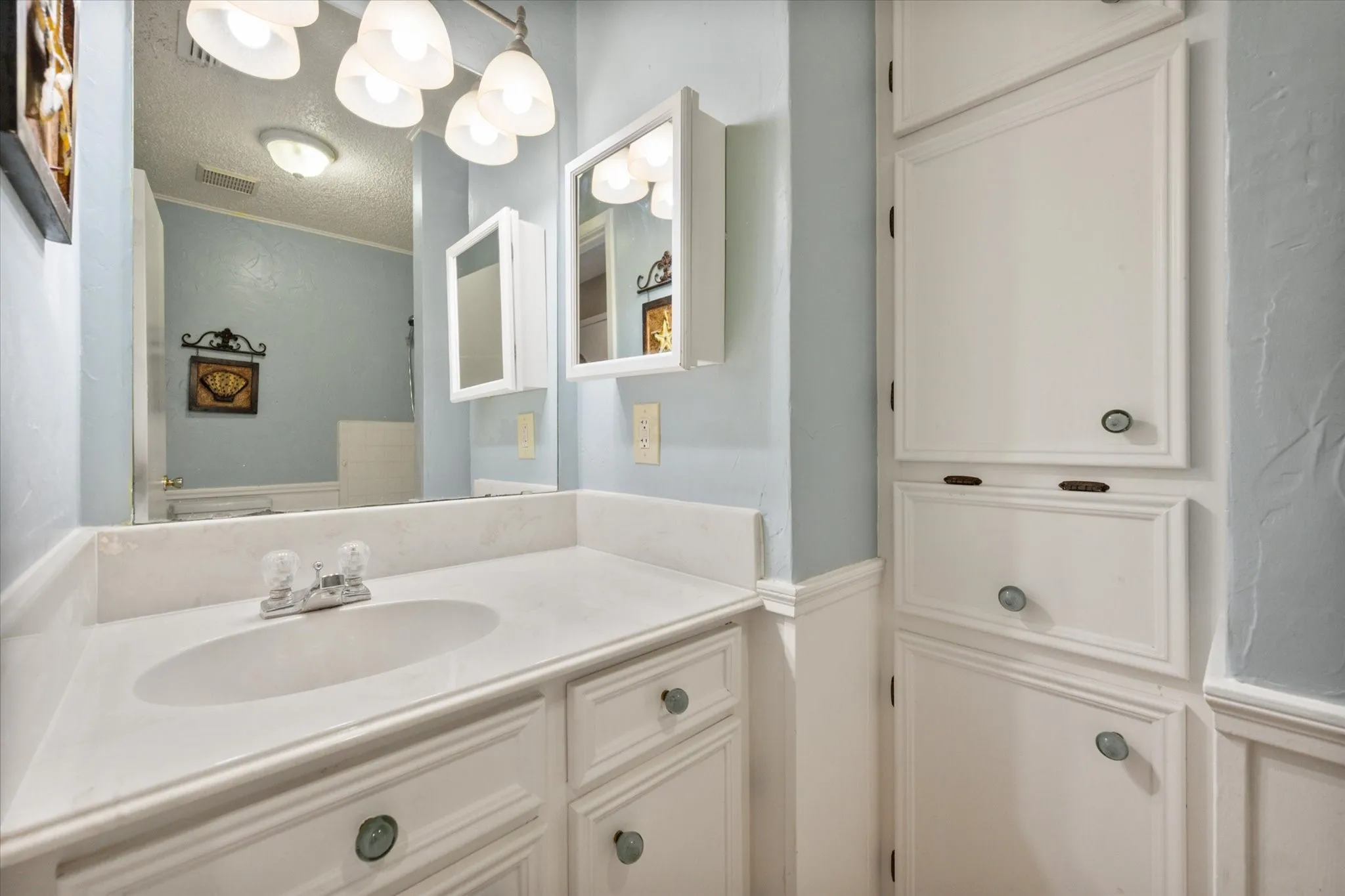 Bathroom featuring a white vanity with an integrated sink, polished chrome faucet, and a large mirror