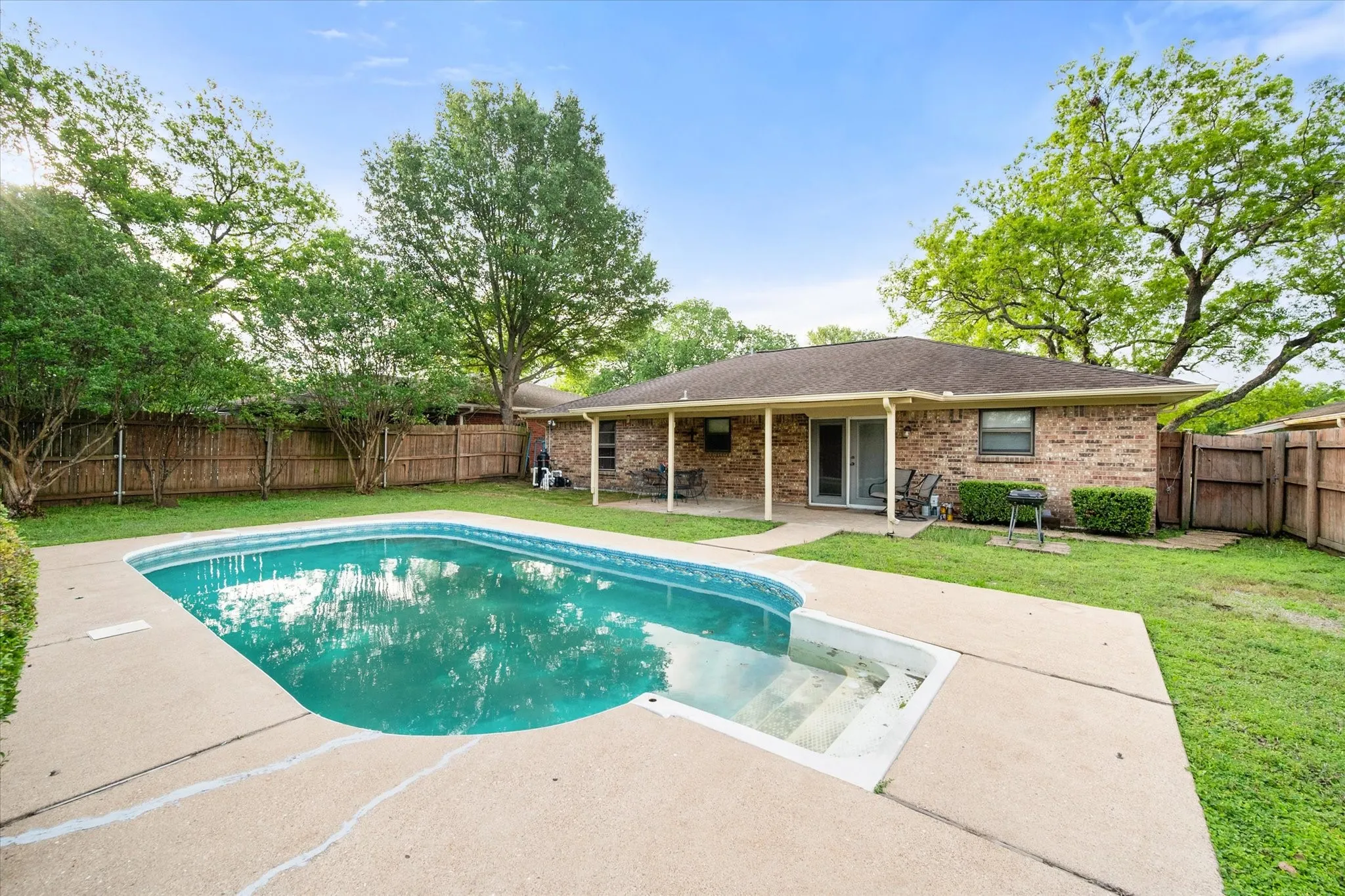 Backyard features a private swimming pool with integrated steps, surrounded by a concrete patio