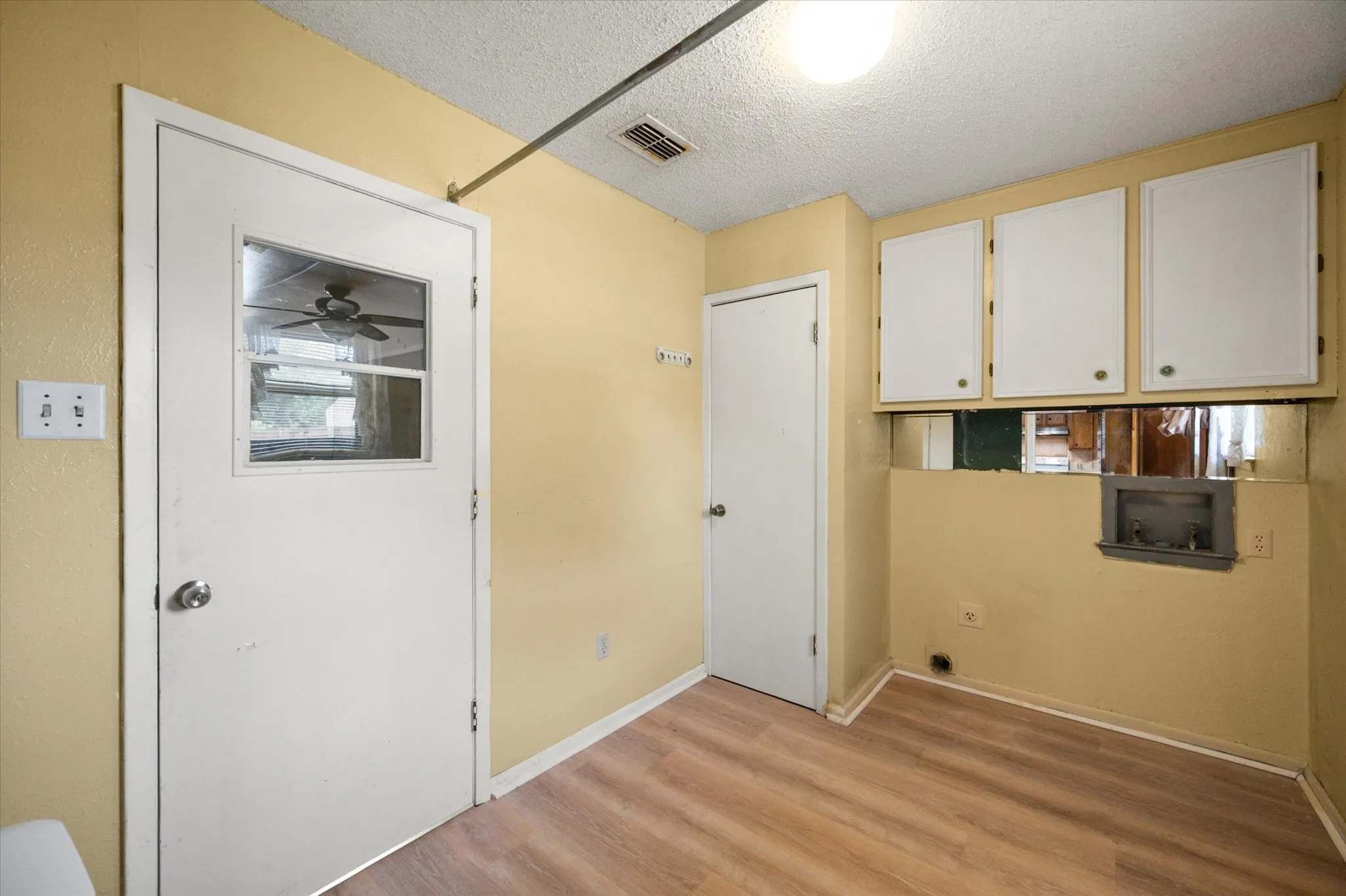 Utility area featuring wood-finish flooring, white cabinetry, and a single light fixture