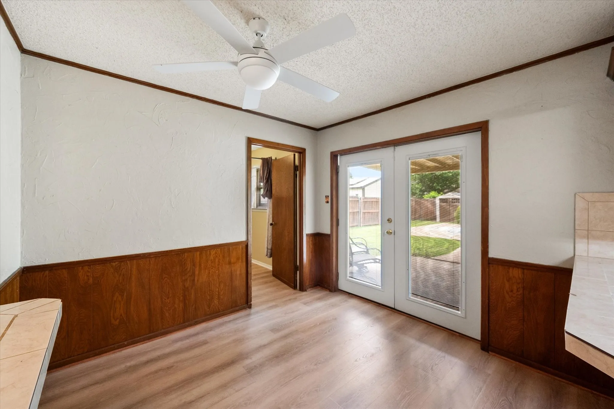 Interior space featuring wood-finish flooring, half-wall wood paneling, and a white ceiling fan