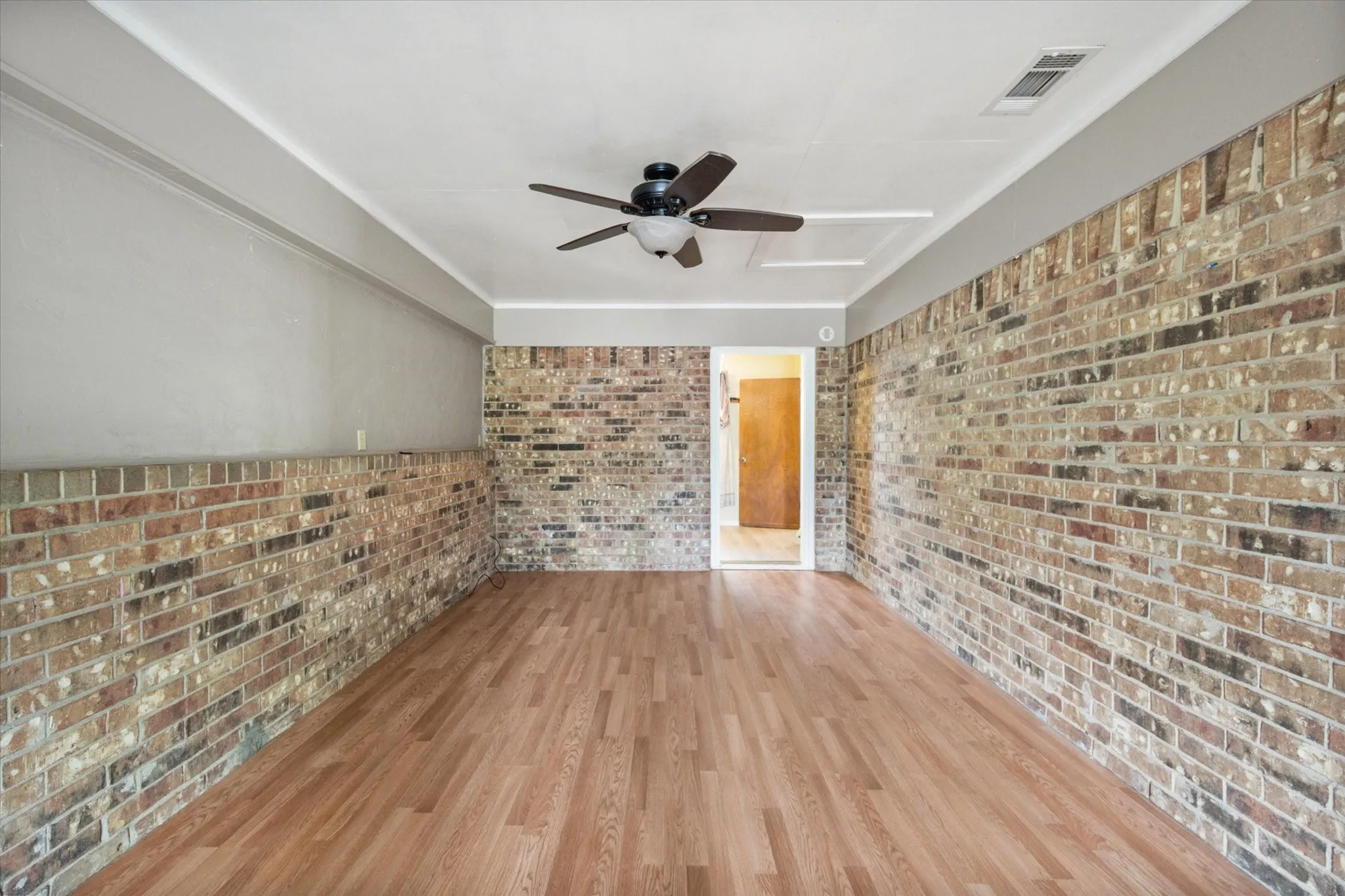 Interior room featuring brick accent walls, wood-finish flooring, a ceiling fan with light fixture, and a white ceiling with crown molding