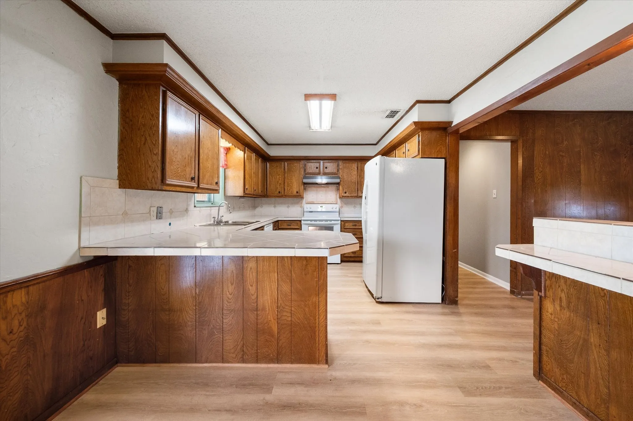 Kitchen featuring wood-finish cabinetry and paneling, light wood-finish flooring, and white tile countertops with a matching backsplash