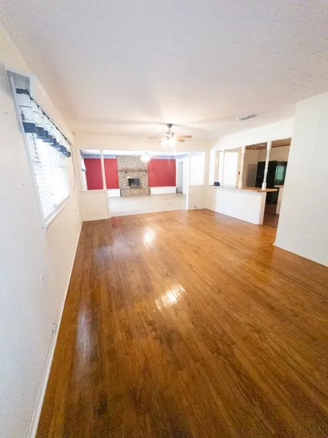 Wood-finish flooring throughout, featuring a stone fireplace, open concept design, and a ceiling fan