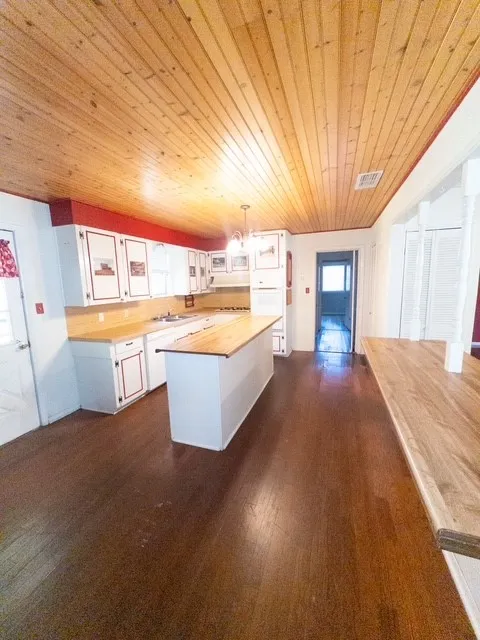 Kitchen featuring a wood plank ceiling, white cabinetry with red trim, wood-finish countertops, a central island, and dark wood-finish flooring