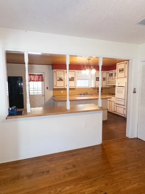 Open concept kitchen with wood-finish flooring, white cabinetry, integrated appliances, and a pass-through bar with turned newel posts