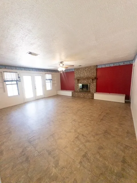 Spacious room featuring neutral-toned tile flooring, a stone-clad fireplace with a mantel, and French doors