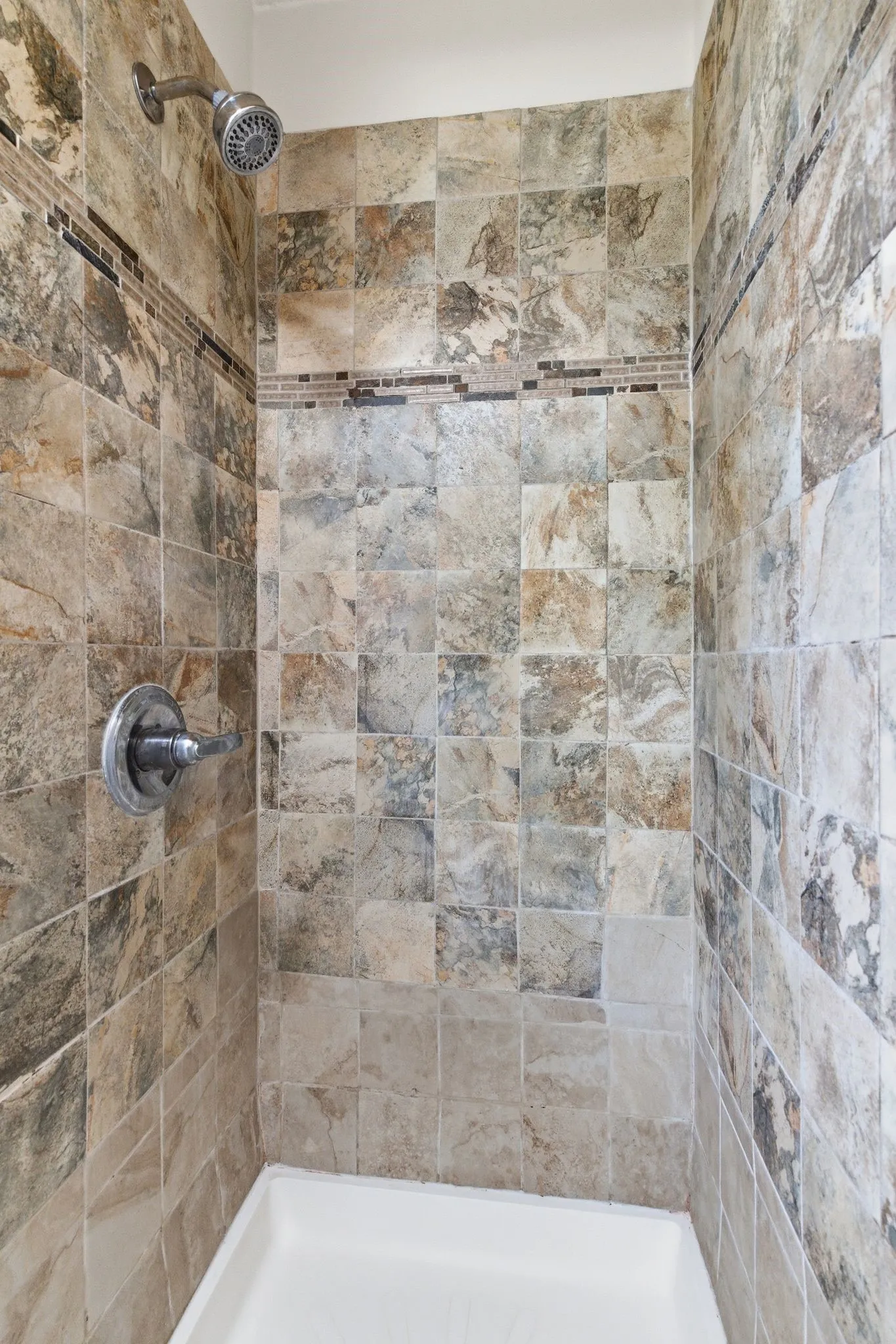 Tiled shower enclosure featuring a mosaic accent band, brushed chrome shower head, and matching control handle