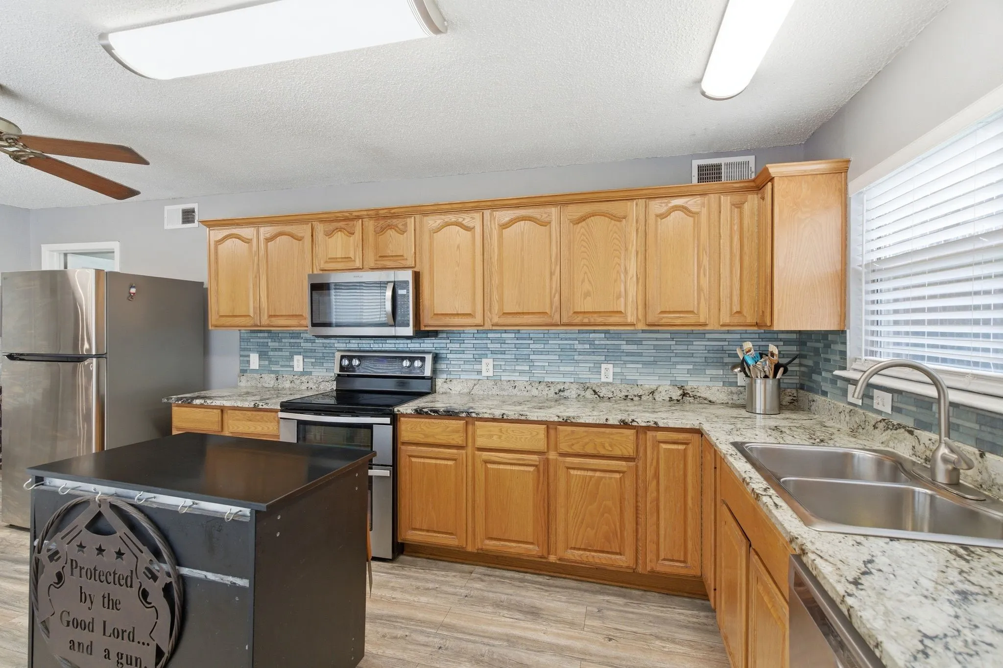 Kitchen featuring a double basin stainless steel sink with gooseneck faucet, light wood cabinetry, a mosaic tile backsplash, and granite countertops
