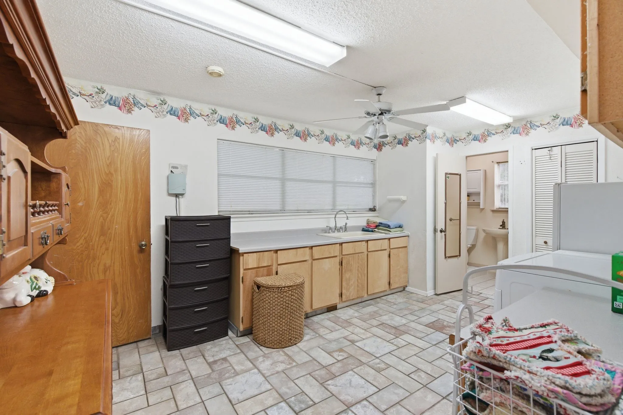 Laundry room featuring tile flooring, a utility sink with an extended countertop, wood-finish cabinetry, and a ceiling fan