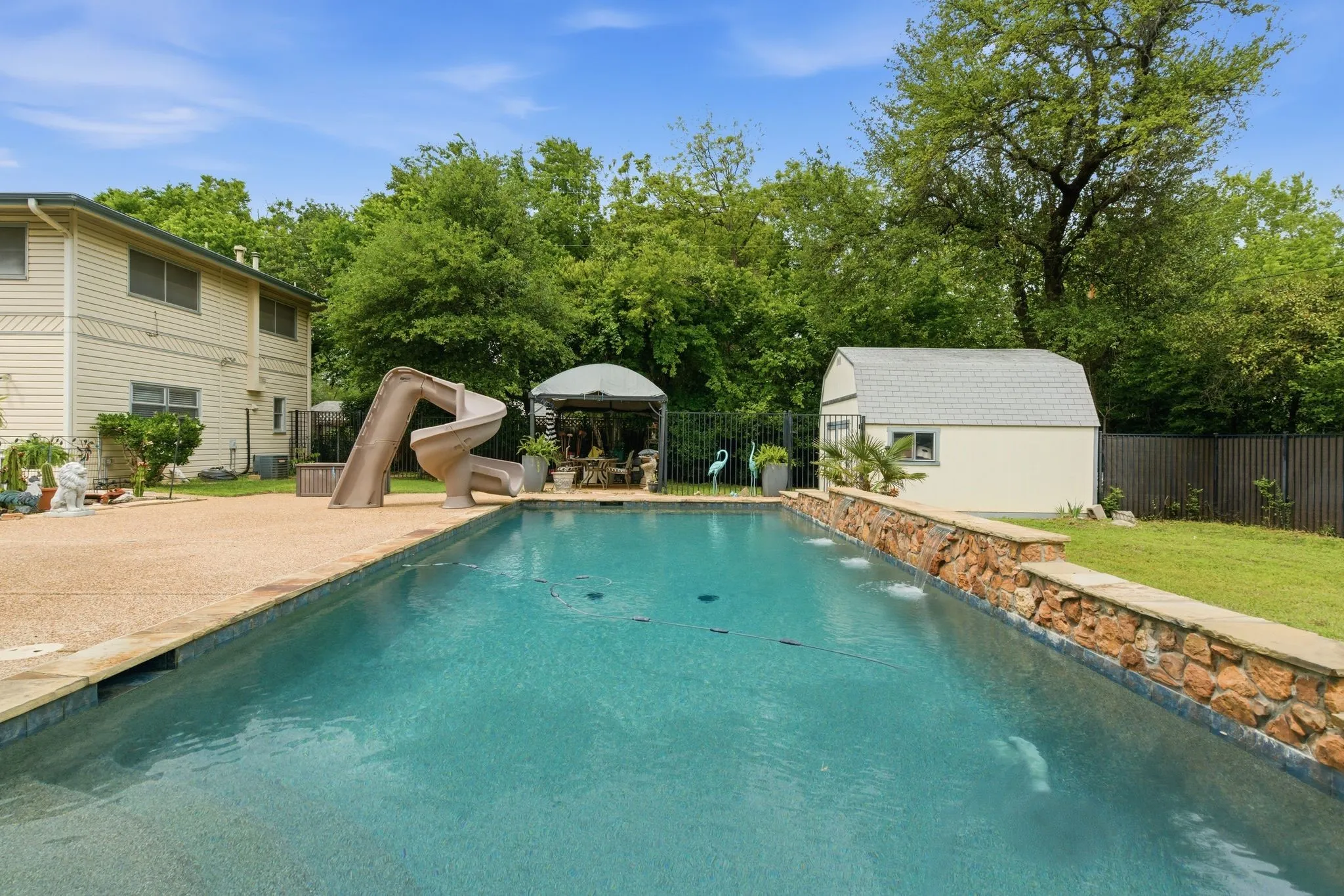 Expansive backyard featuring a rectangular swimming pool with stone coping, a built-in water slide, and a covered gazebo