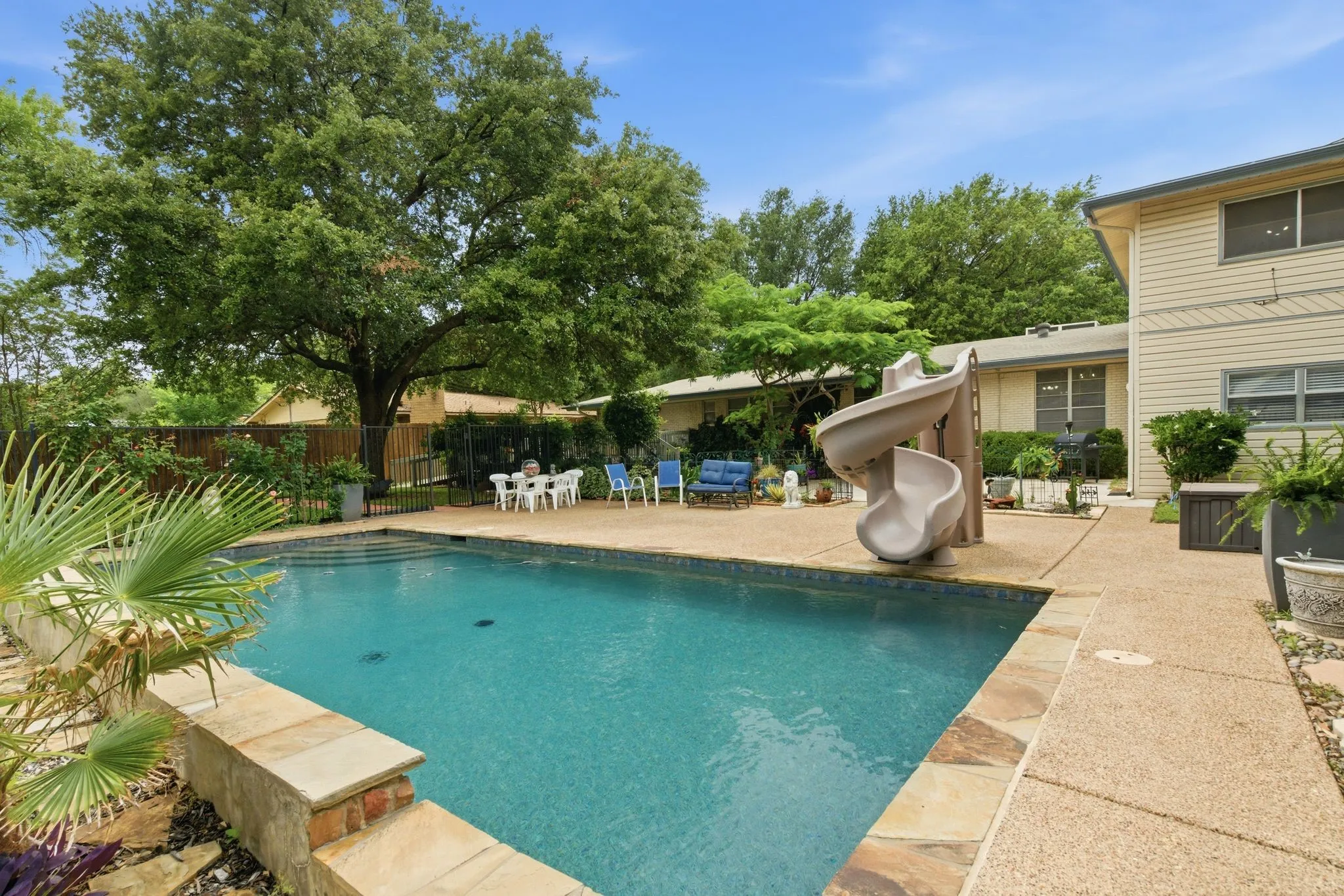 Expansive backyard featuring a rectangular swimming pool with a stone coping and a concrete surround